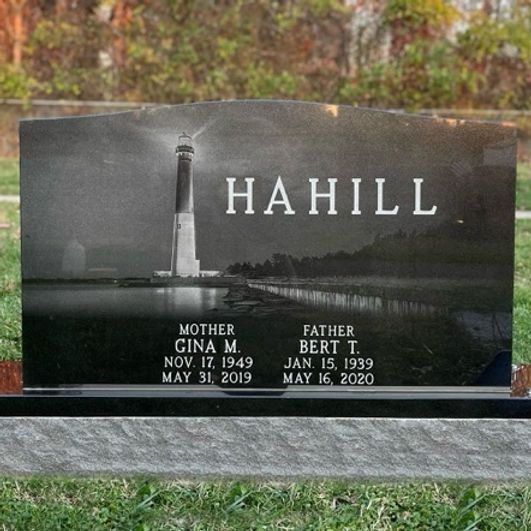 A black gravestone with a laser etching of a lighthouse reflecting on the water in the foreground