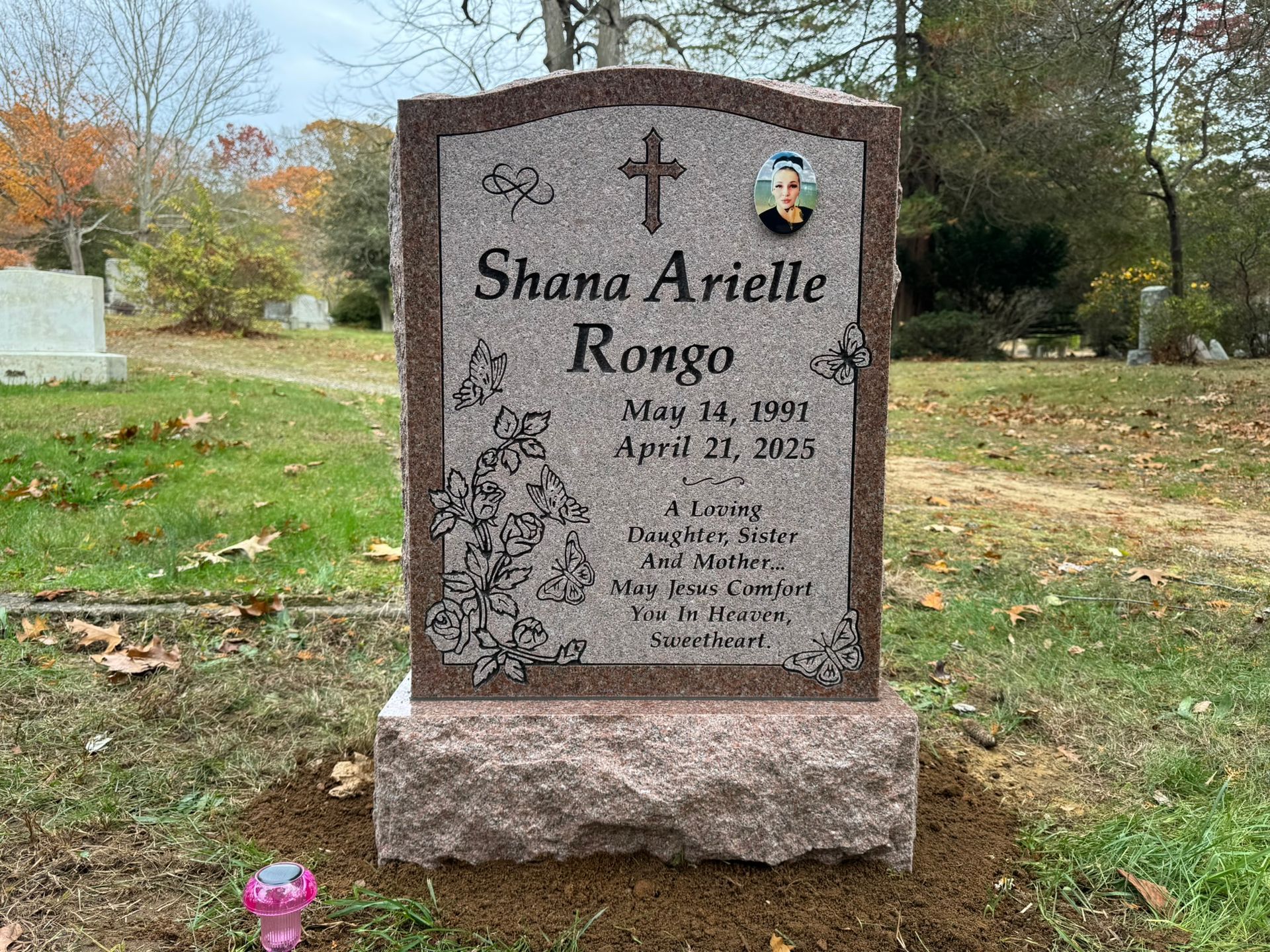 Grave marker. Pink granite with cross and floral details.