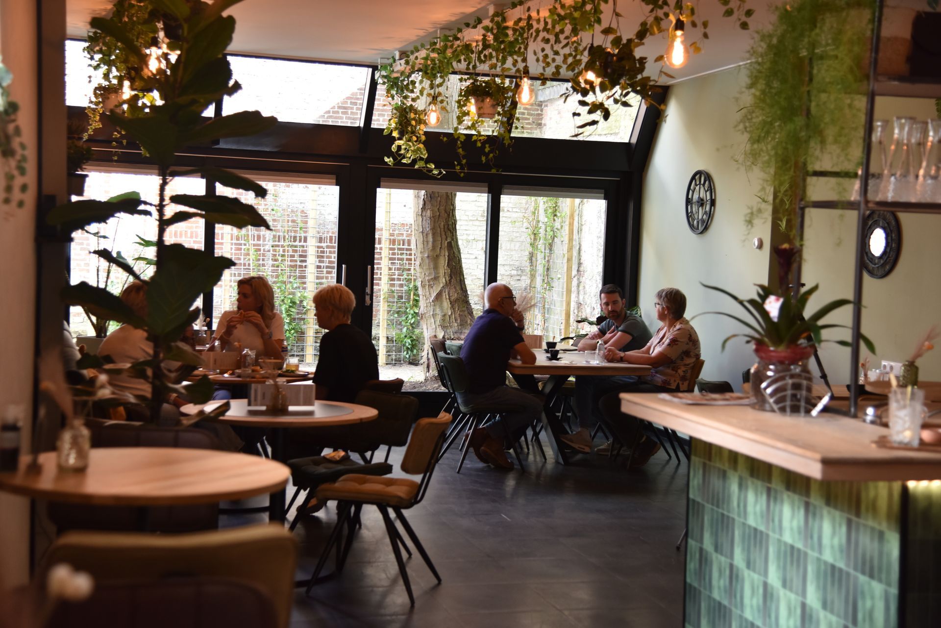 Interieur van lunchroom de tweeling met gasten aan tafel, weelderig groen en een bar.