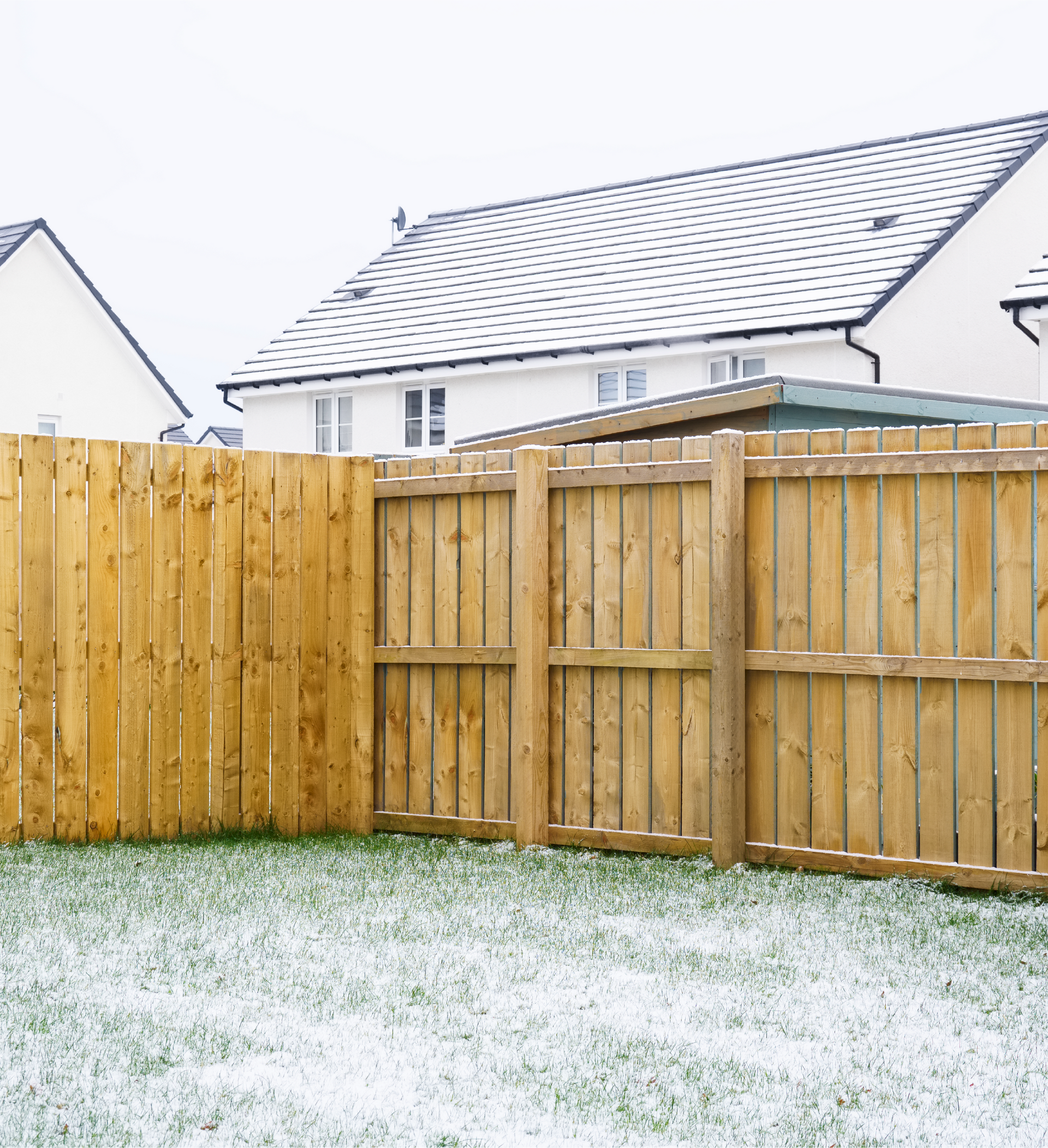 A wooden fence in front of a house with snow on the ground