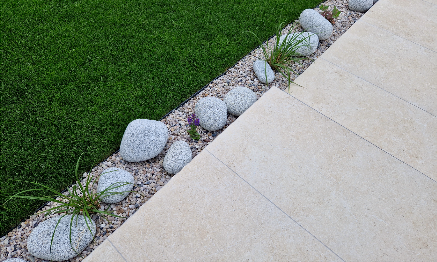 A stone walkway surrounded by rocks and grass next to a lawn.