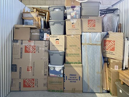 Storage unit filled with boxes and plastic bins, stacked floor to ceiling.