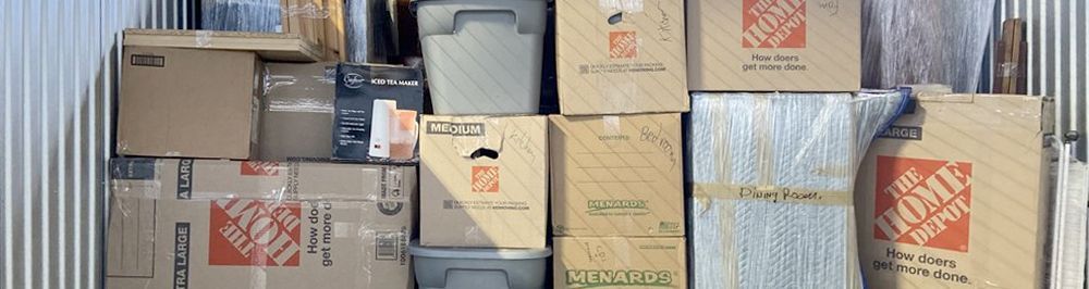 Boxes stacked inside a storage unit. Various sizes of cardboard boxes, and plastic bins.