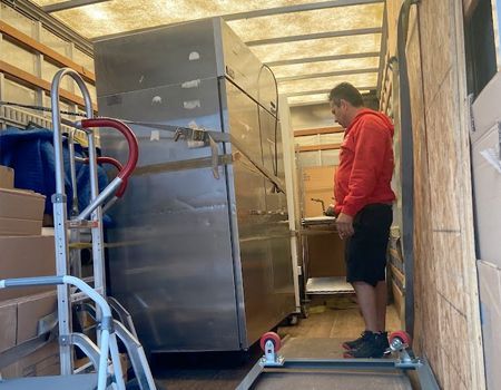 Man in red shirt inside truck near a large, metal object on a dolly.