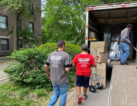 Movers loading boxes into a truck, next to a building. Two men walking with boxes.