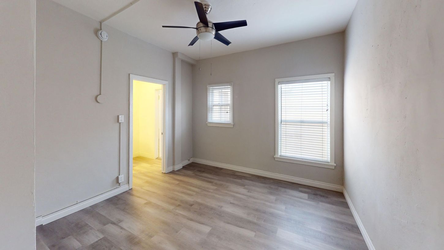 Empty room with gray walls, wood-look floor, windows, and ceiling fan.