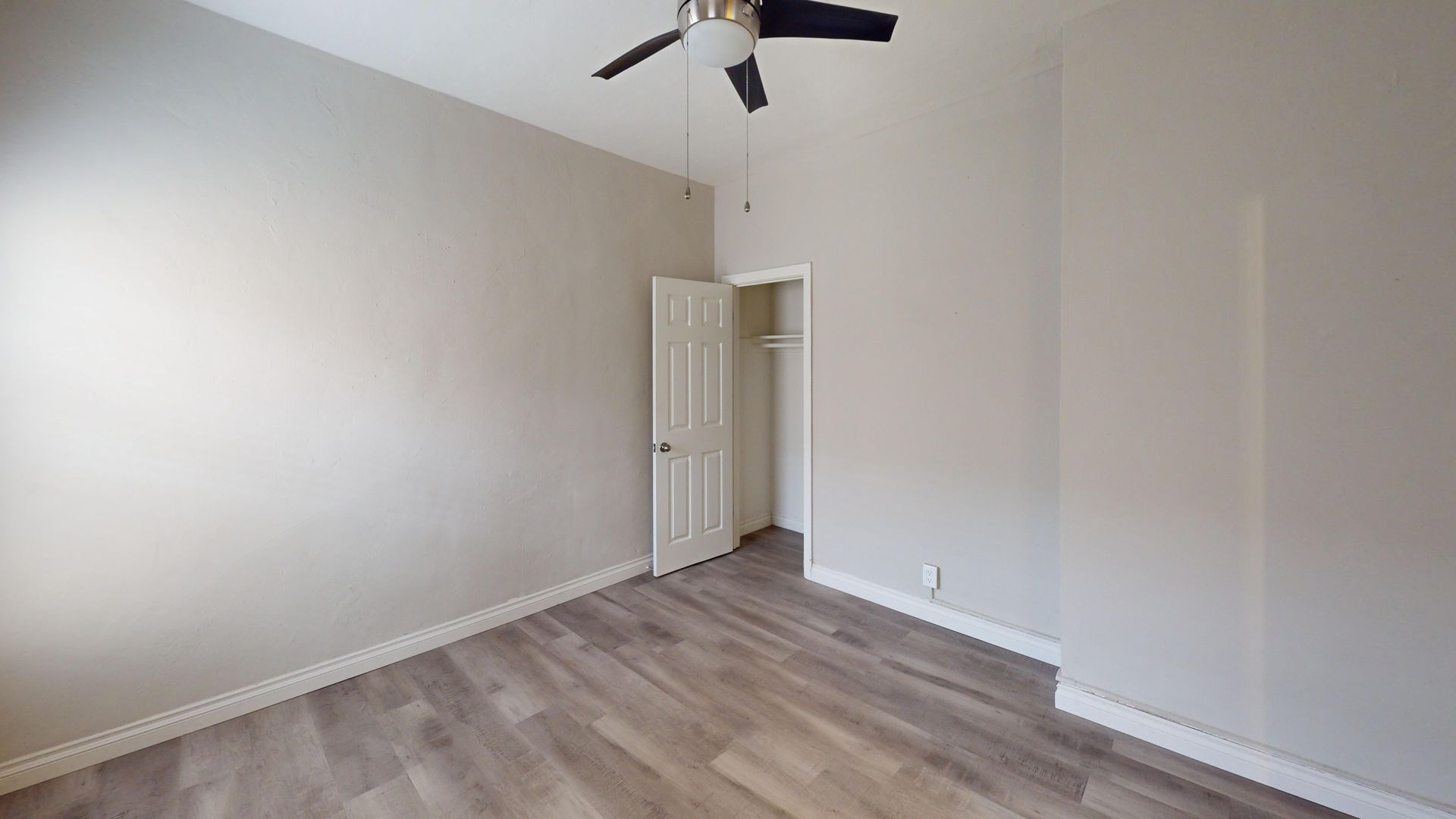 Empty room with gray walls, wood-look flooring, closet, and ceiling fan.