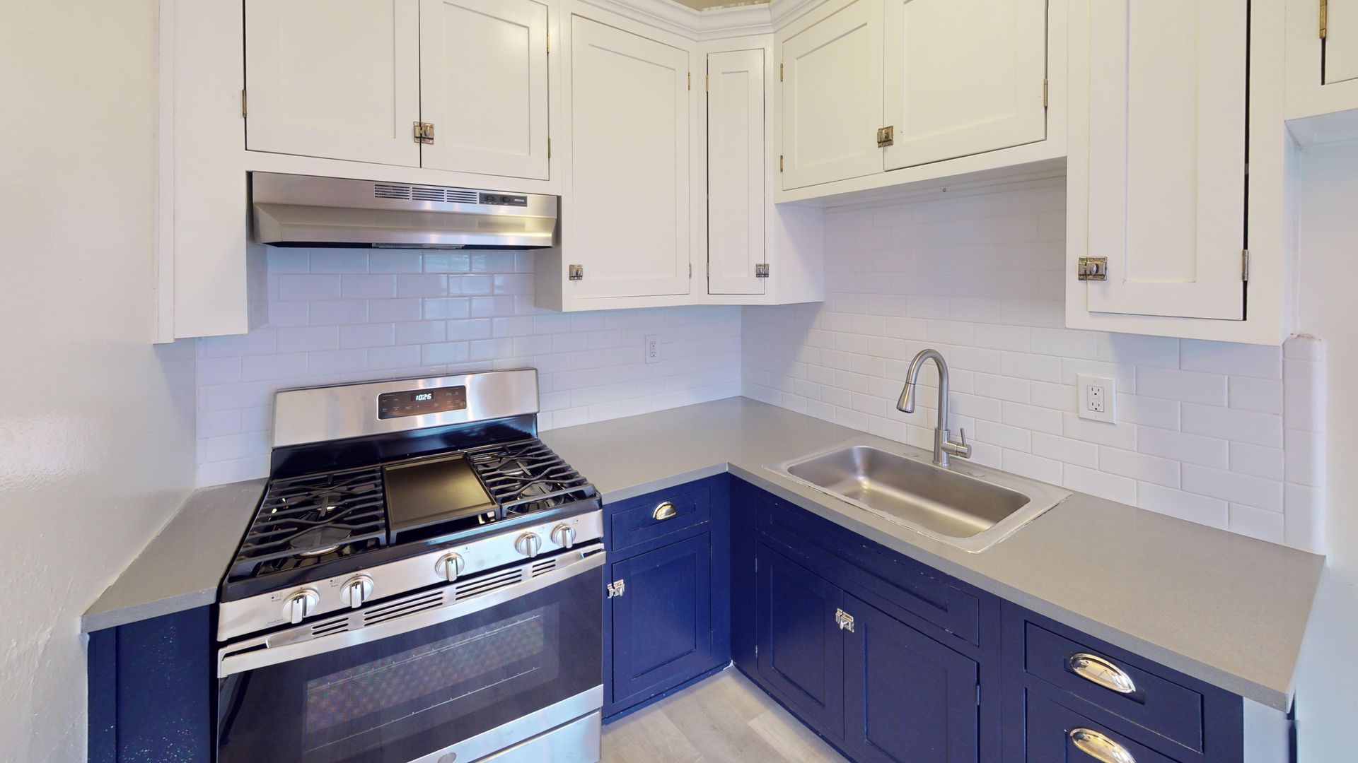 A renovated kitchen with blue and white cabinets, stainless steel appliances, and a gray countertop.