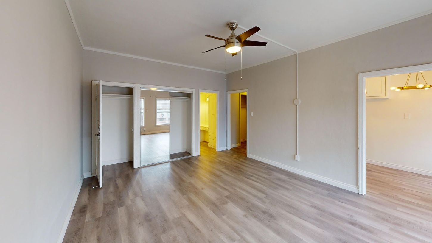 Empty room with gray walls, wood-look floors, ceiling fan, open closet, and doorways.