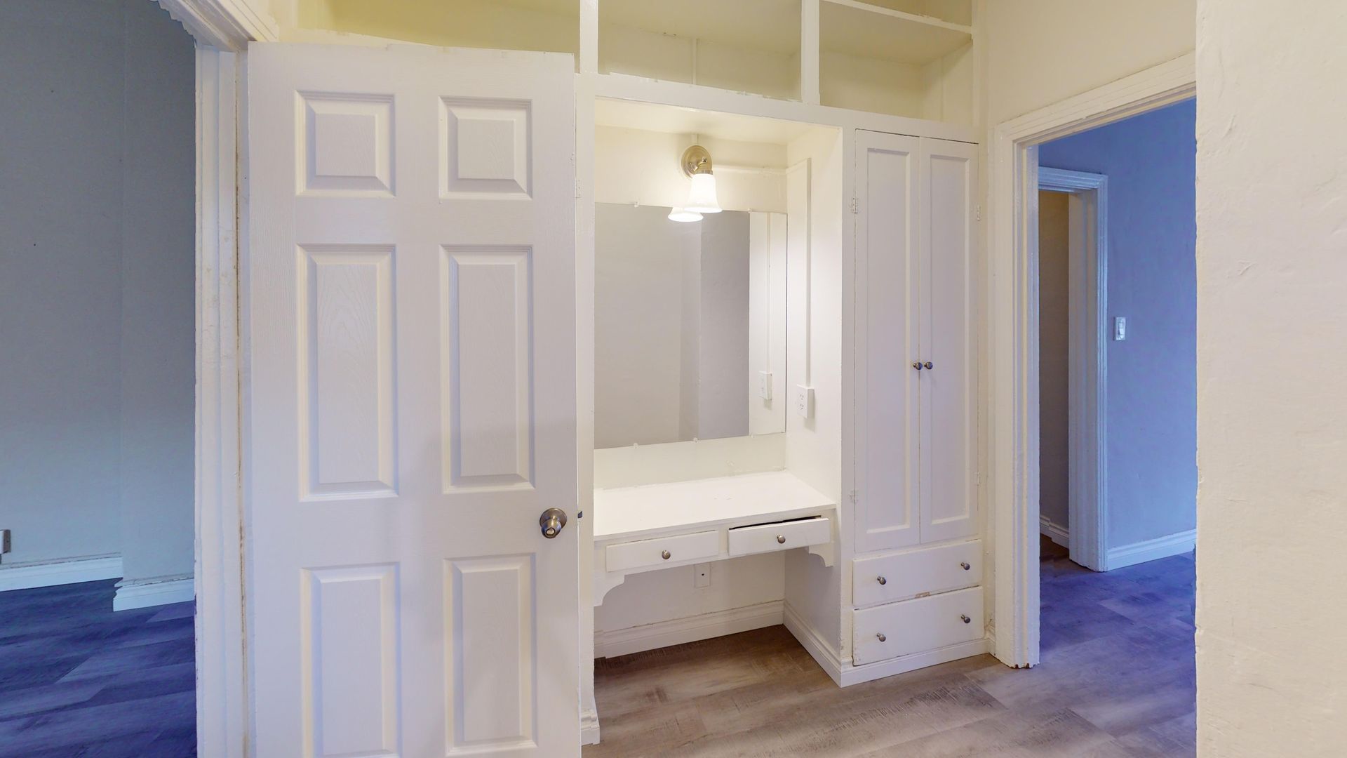 White built-in vanity with a mirror and drawers, flanked by cabinet doors and shelves, in a bedroom.