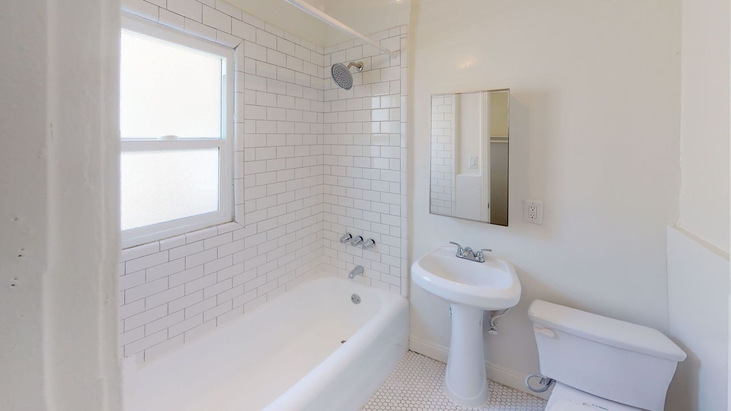 White bathroom with a bathtub, toilet, sink, and window.