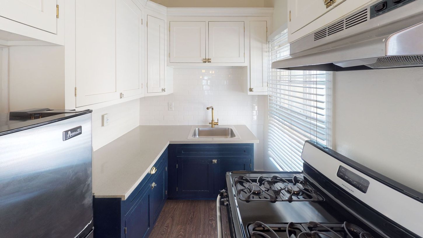 Small kitchen with white upper cabinets, navy blue lower cabinets, and stainless steel appliances.