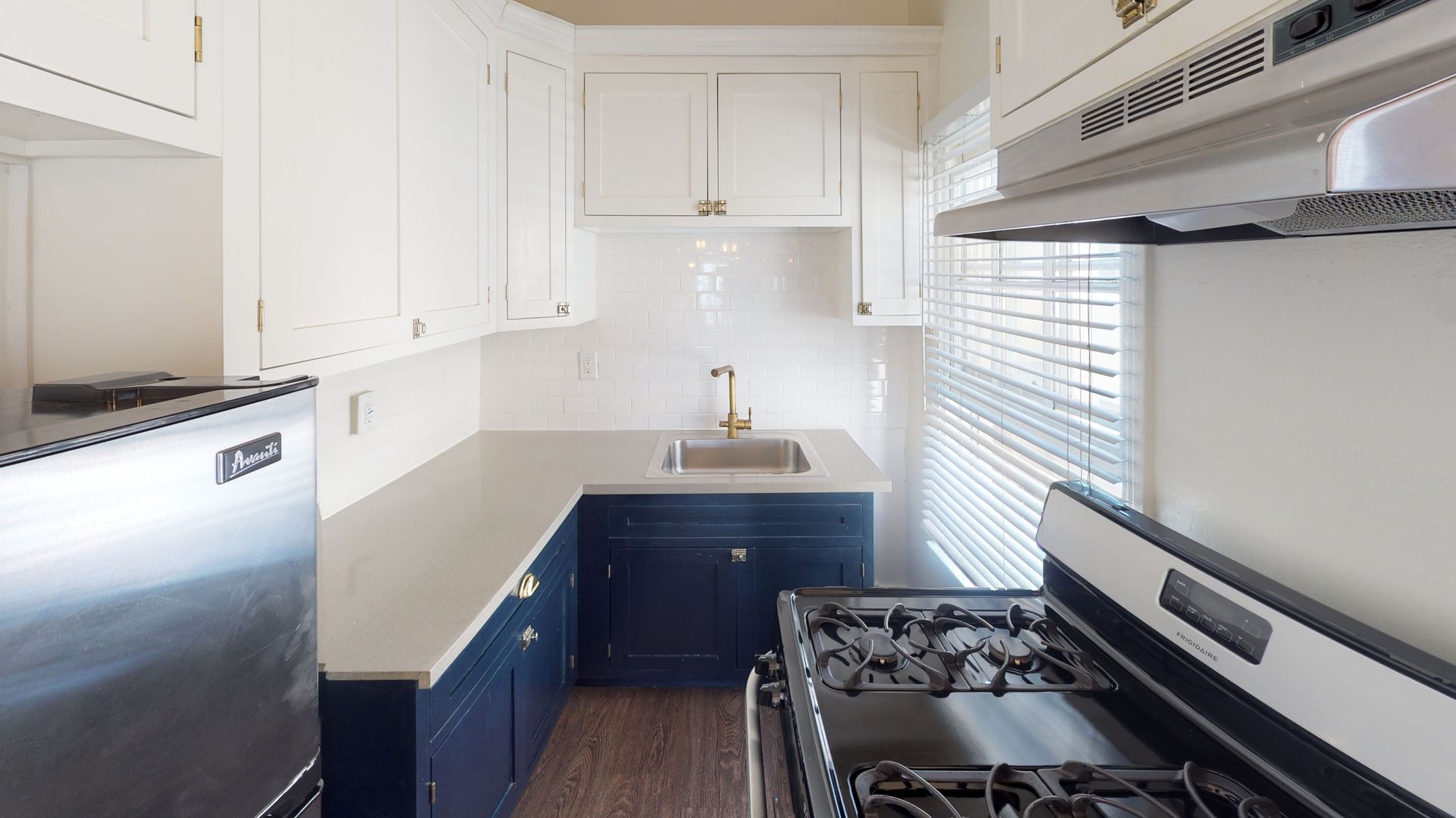 Small kitchen with white upper cabinets, navy blue lower cabinets, and stainless steel appliances.