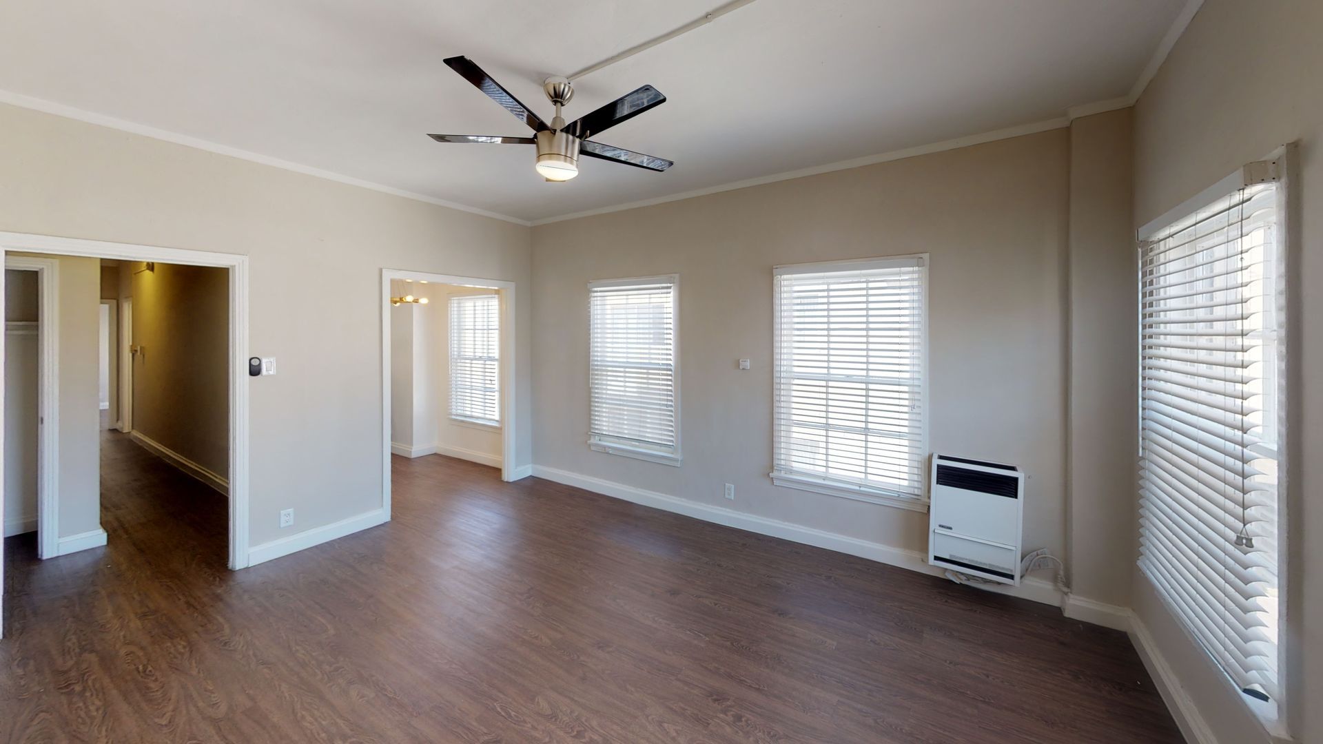 Empty living room with wood flooring, three windows, and a ceiling fan.