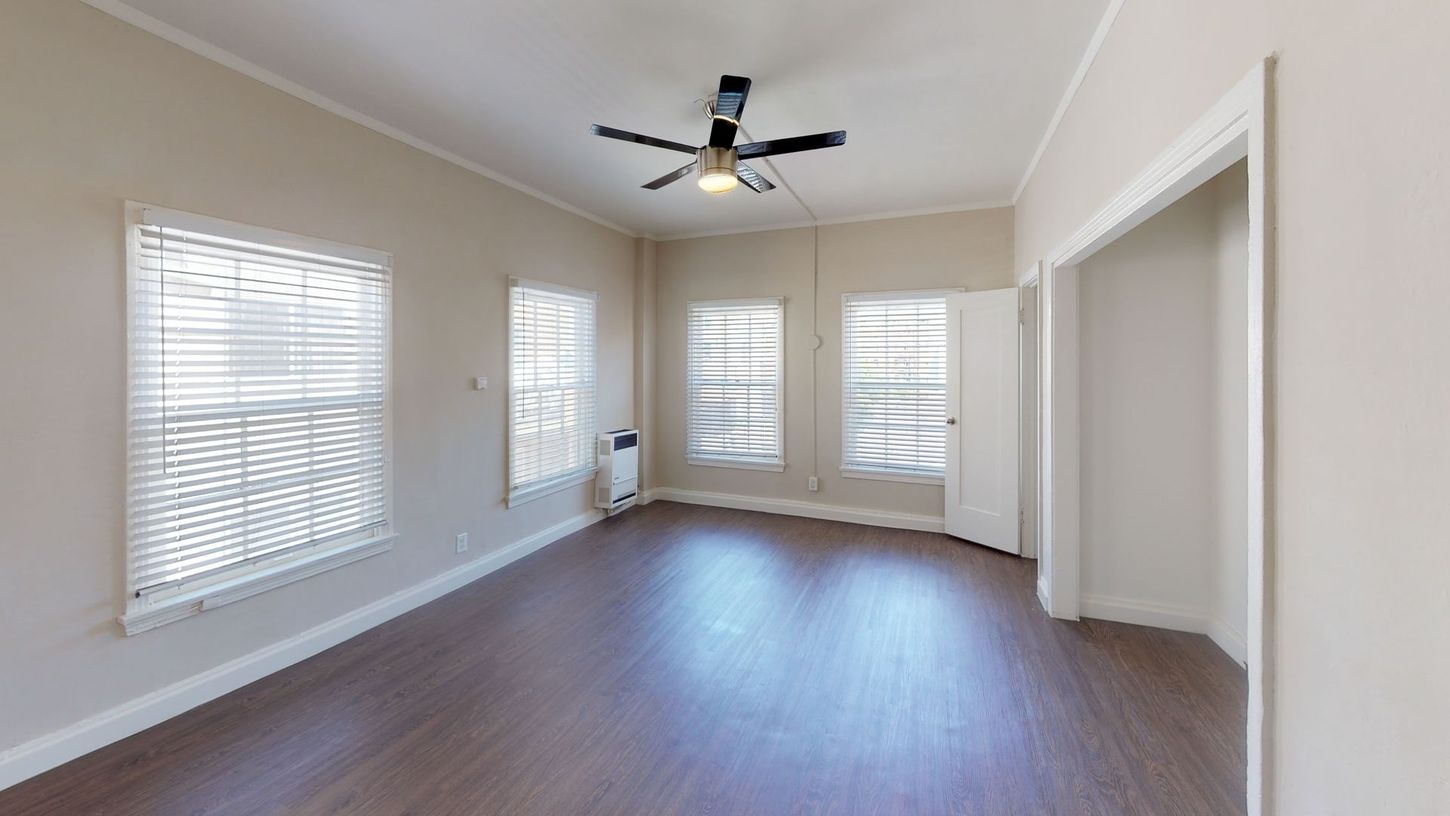 Empty room with dark wood floor, windows with blinds, and a ceiling fan.