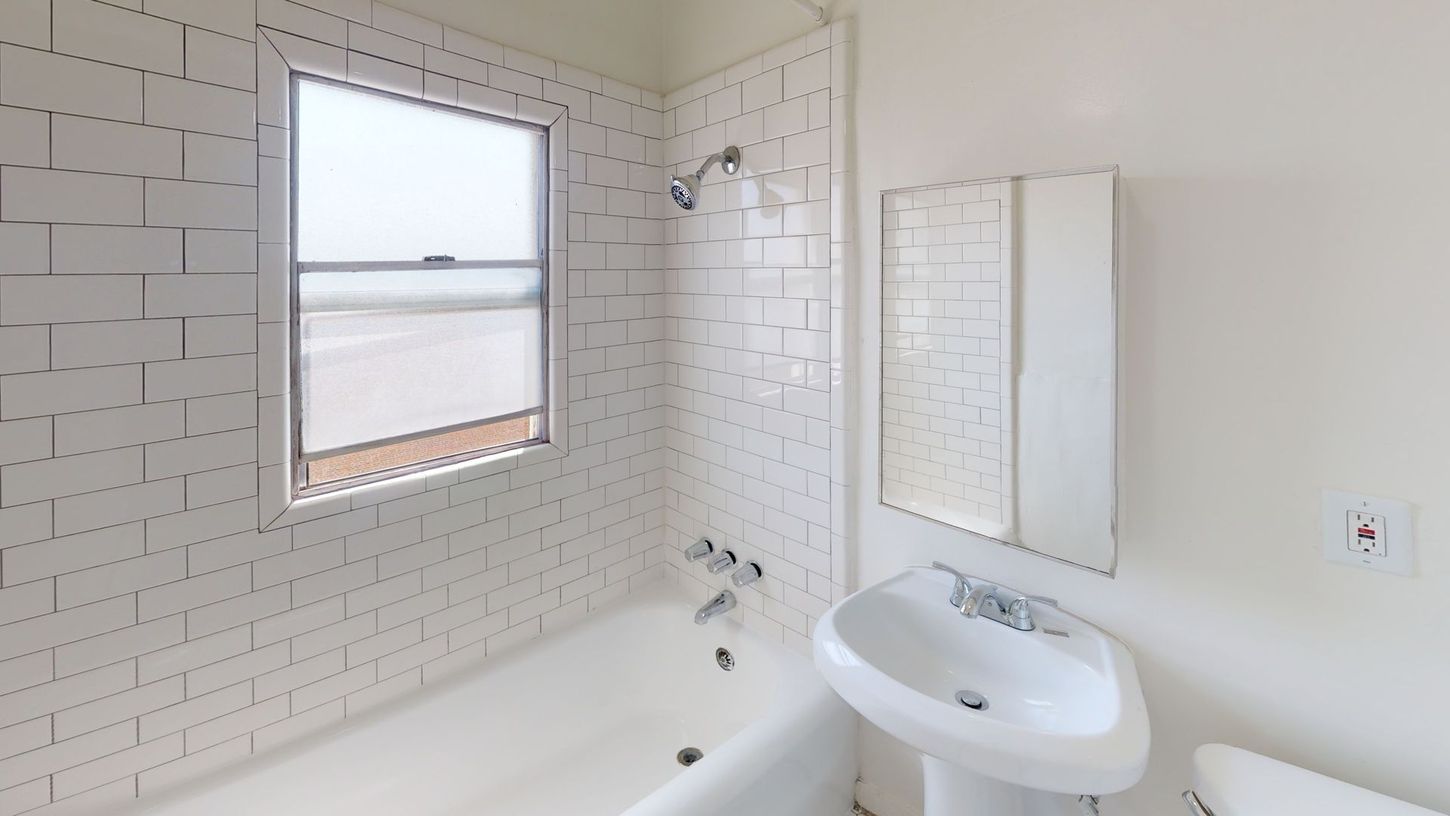 White bathroom with subway tile, window, tub, pedestal sink, and medicine cabinet.