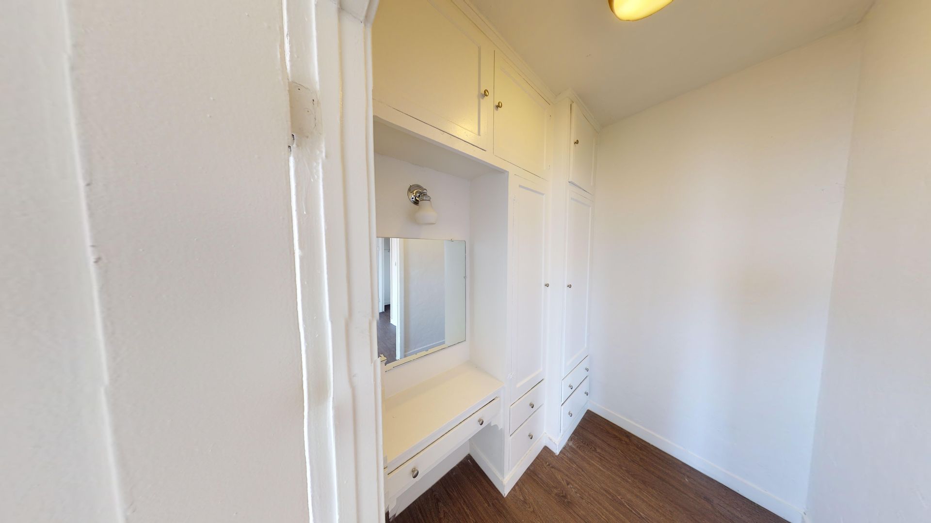 White dressing room with built-in cabinets and a vanity with a mirror. Dark wood floor.