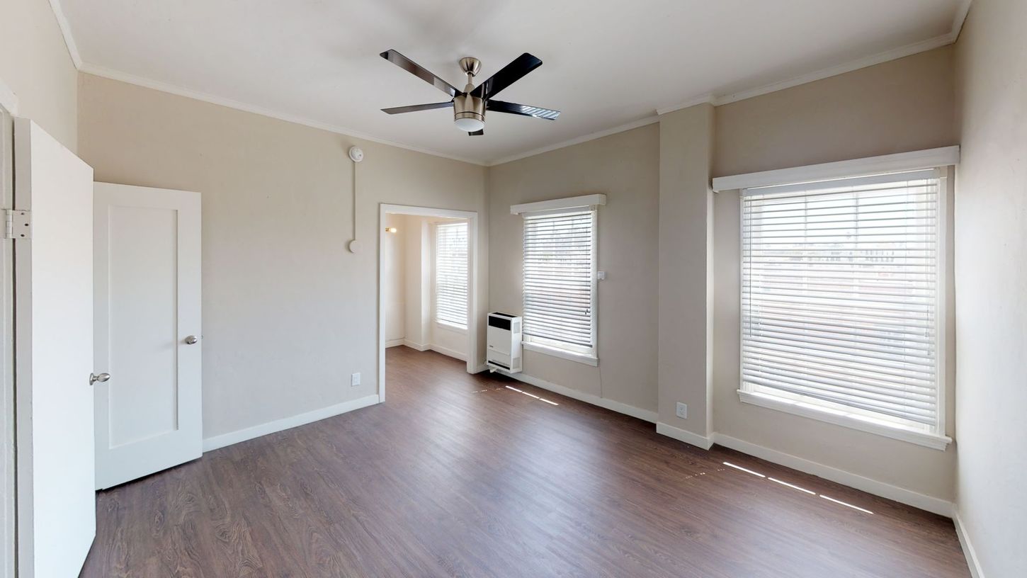 Empty room with brown floors, windows, ceiling fan, and white walls.