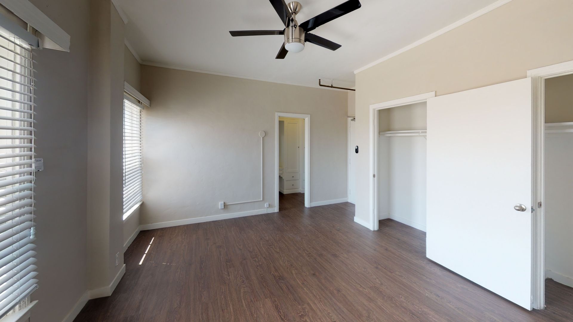 Empty bedroom with brown wood floor, white closet doors, and a ceiling fan.