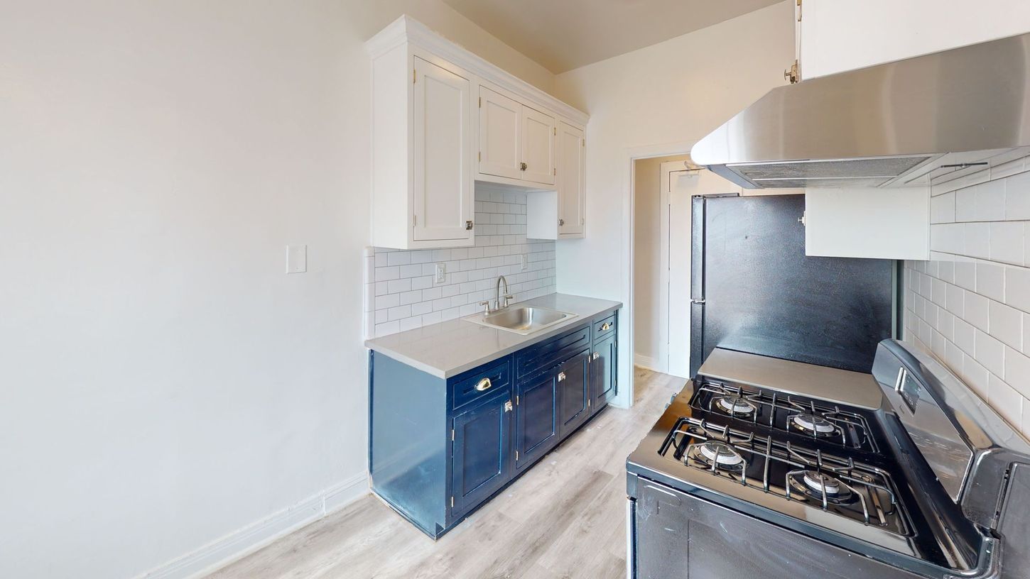 Kitchen with white upper cabinets, blue lower cabinets, and a black stove.