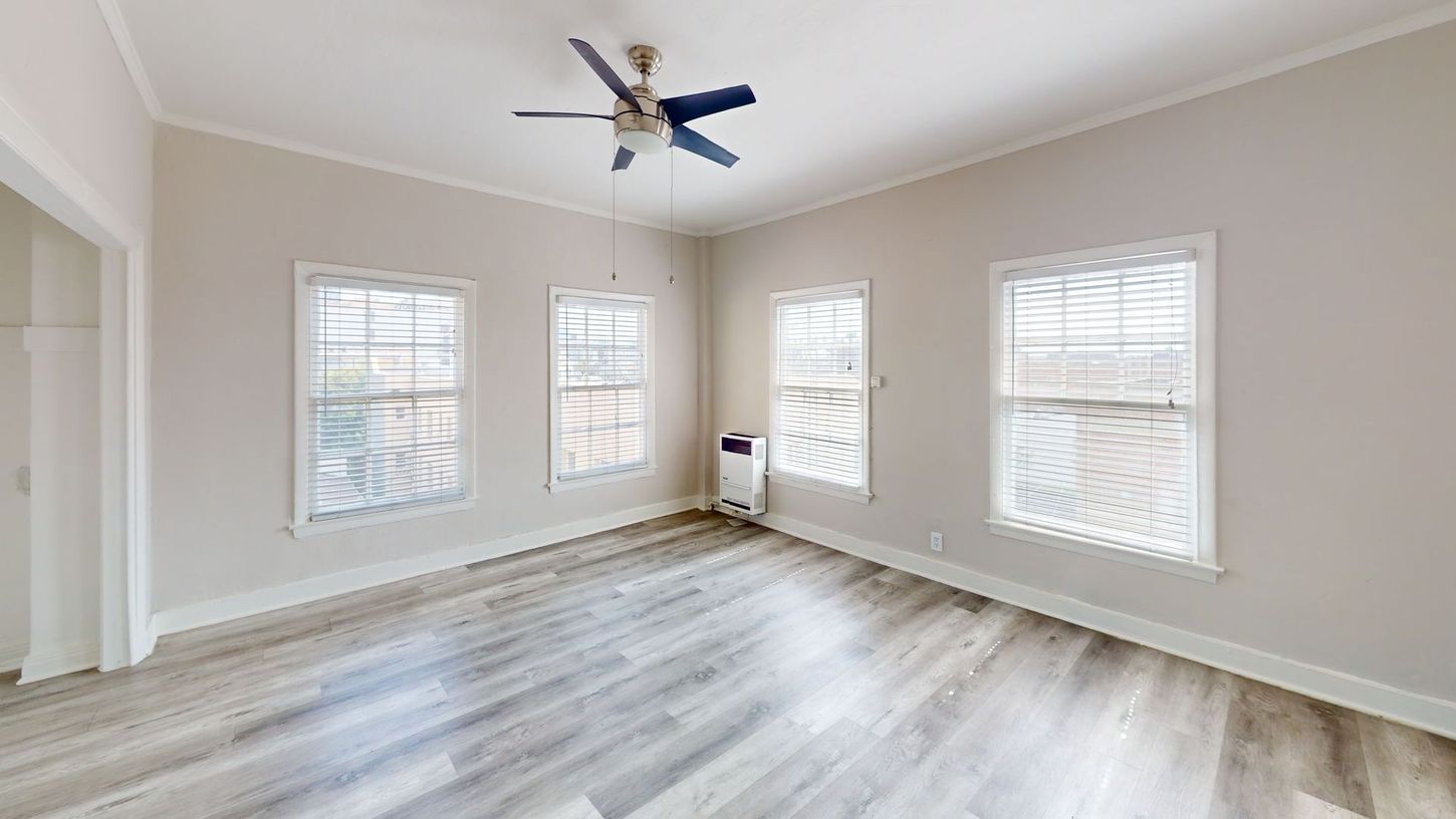 Empty room with three windows, gray flooring, and a blue ceiling fan.