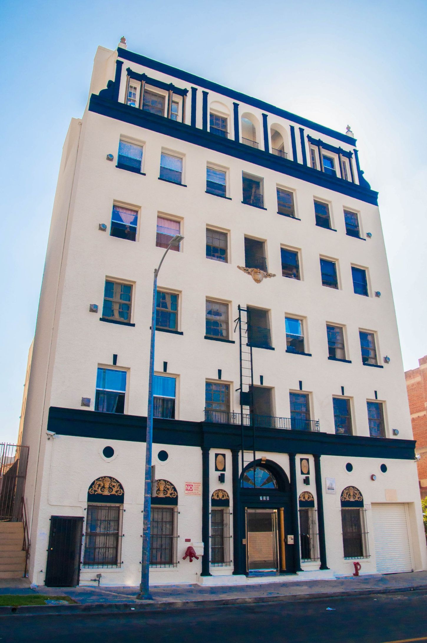 Six-story white apartment building with black trim, arched entrance, and street-level windows on a sunny day.