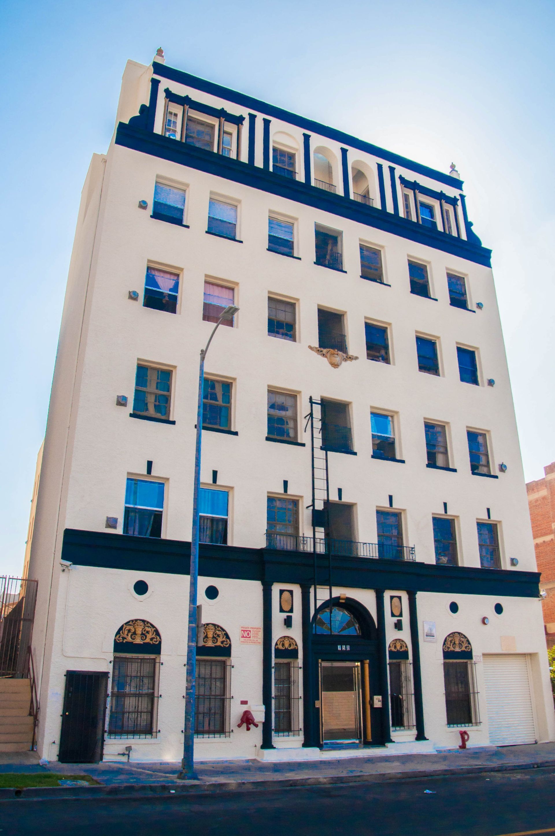 Six-story white apartment building with black trim, arched entrance, and street-level windows on a sunny day.