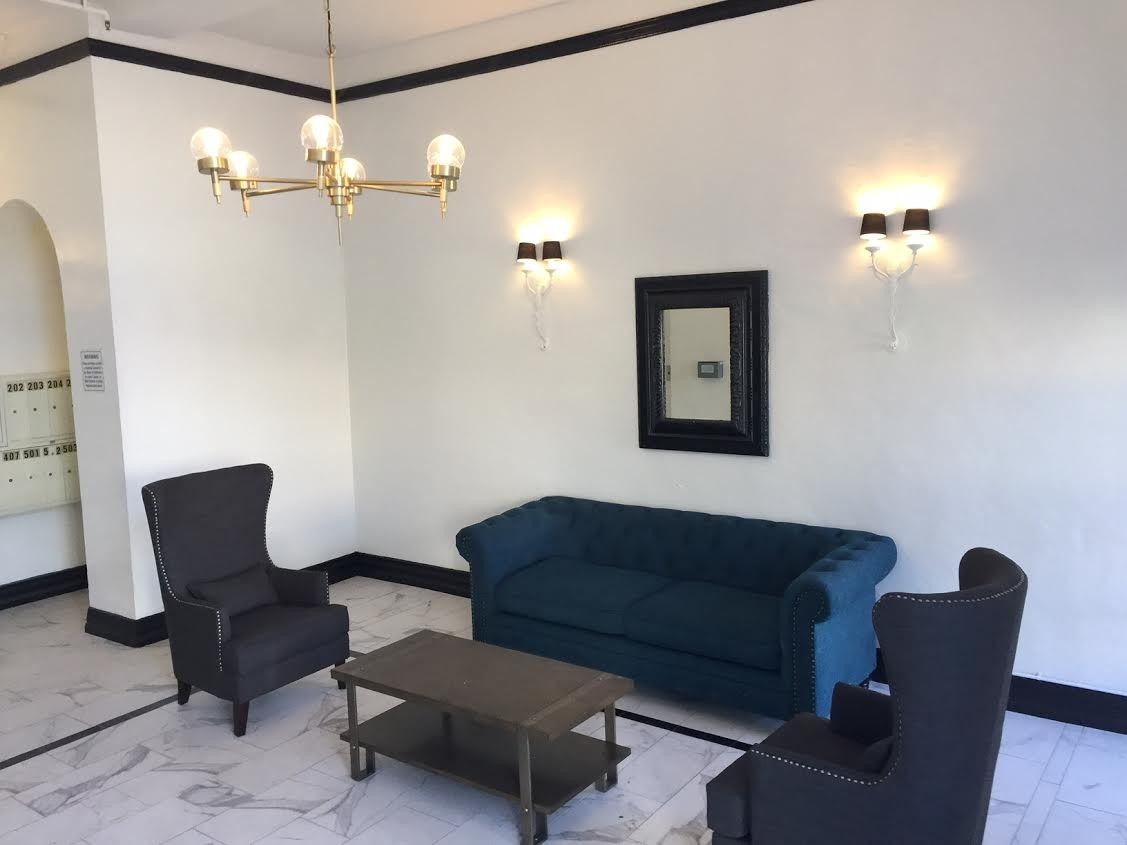 Lobby with blue sofa, two armchairs, coffee table, chandelier, sconces, and a mirror on a marble floor.