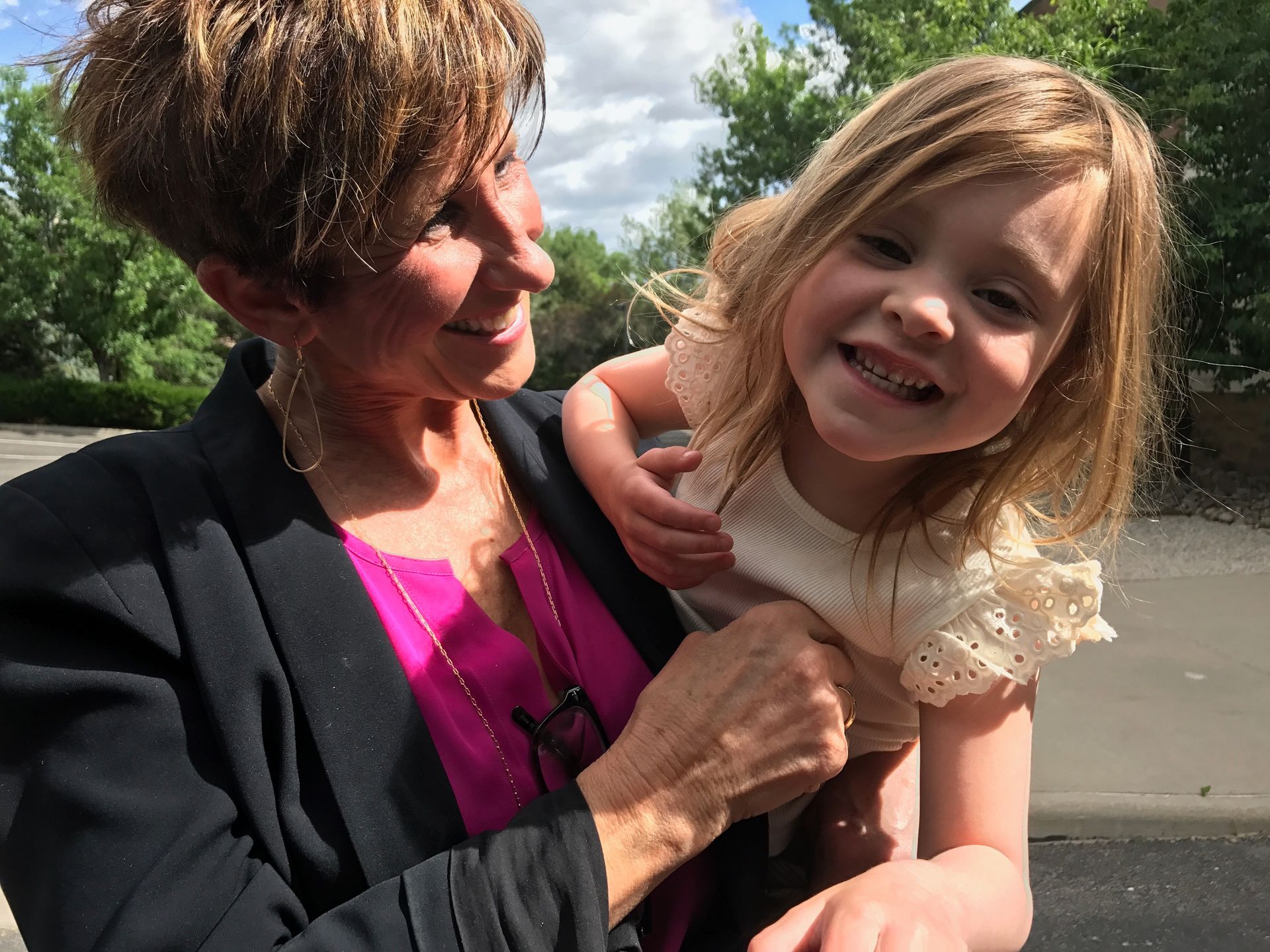 Woman holding a smiling child outdoors. Both are looking at the camera.