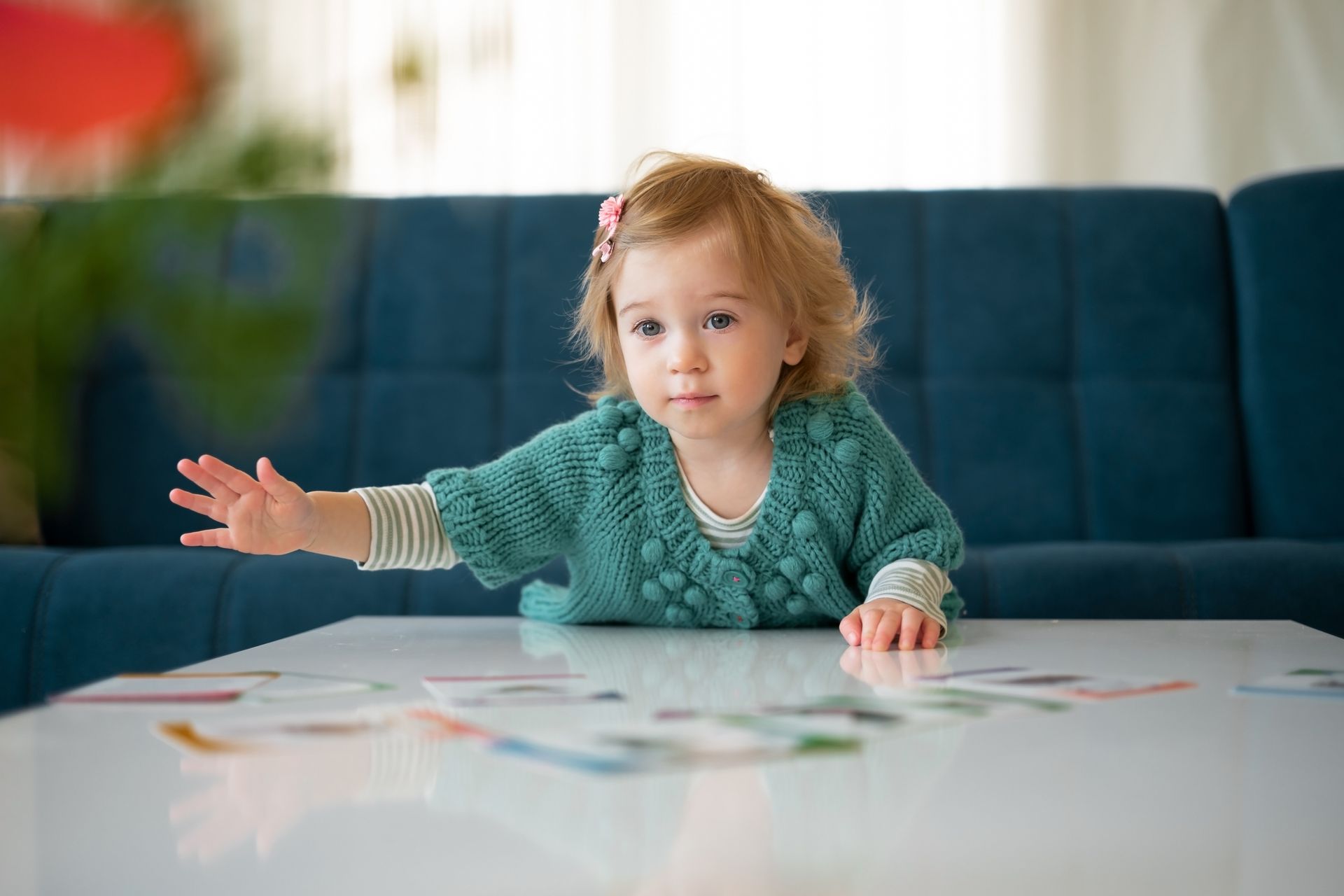 Child in teal sweater leans over table, reaching for colorful cards.