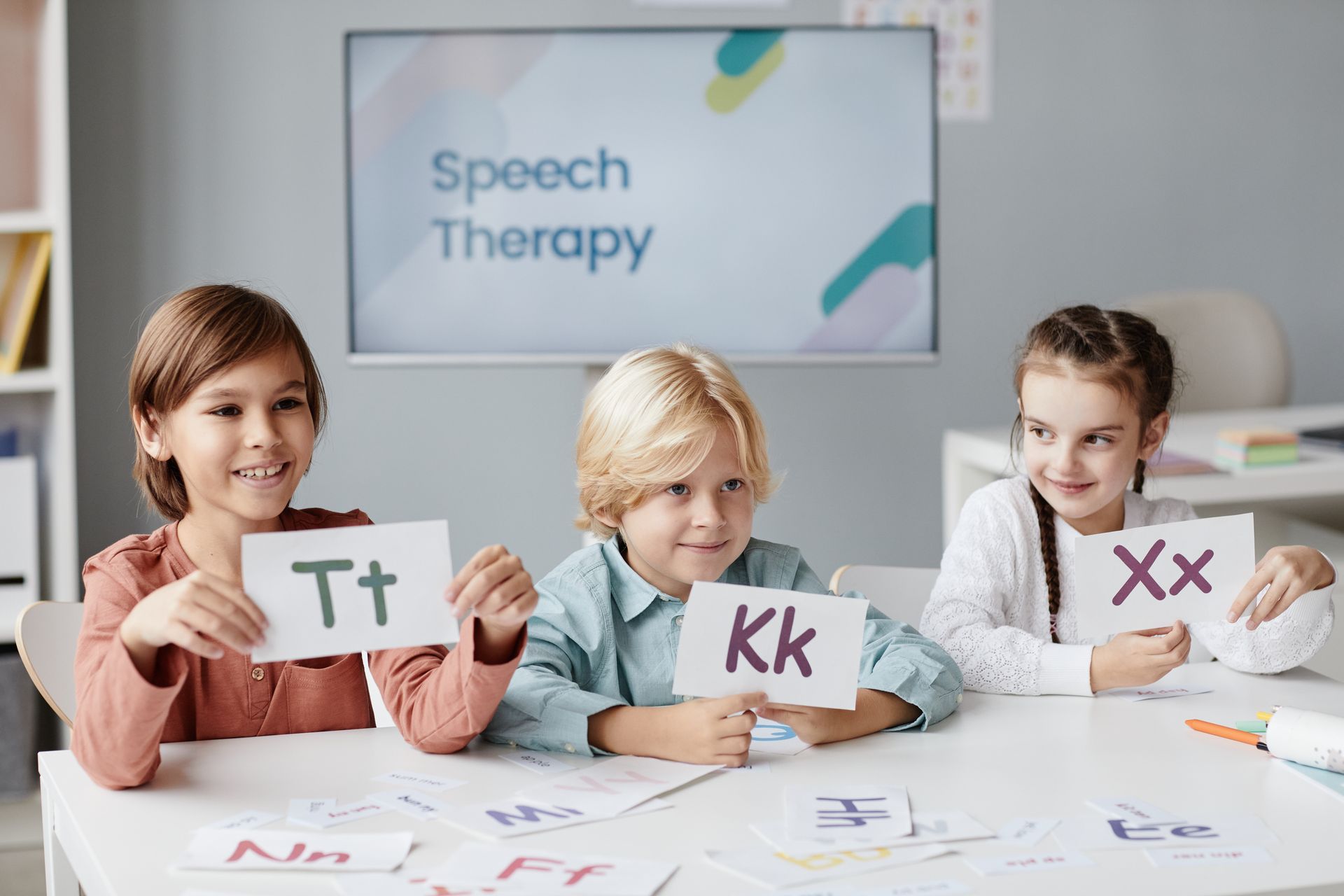 Three children holding letter cards at a speech therapy session;