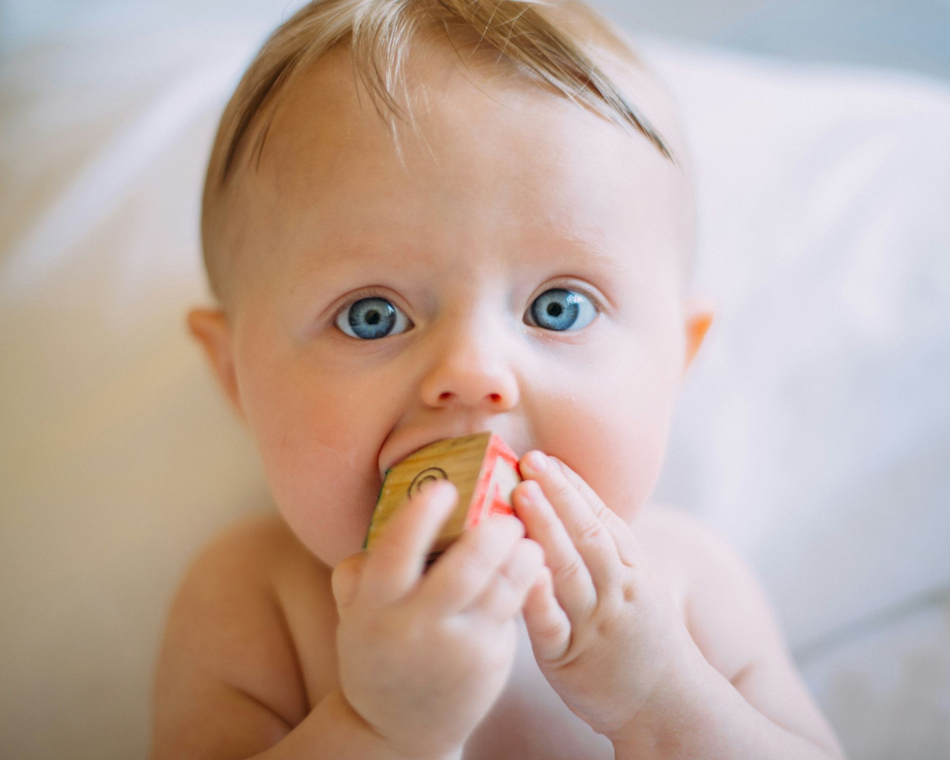 Baby with blue eyes, biting a wooden block.