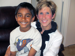 Smiling woman and boy seated close together indoors. The boy wears a printed t-shirt.