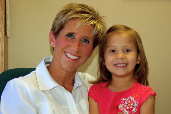 Woman with short blonde hair and girl in red shirt smiling close together.