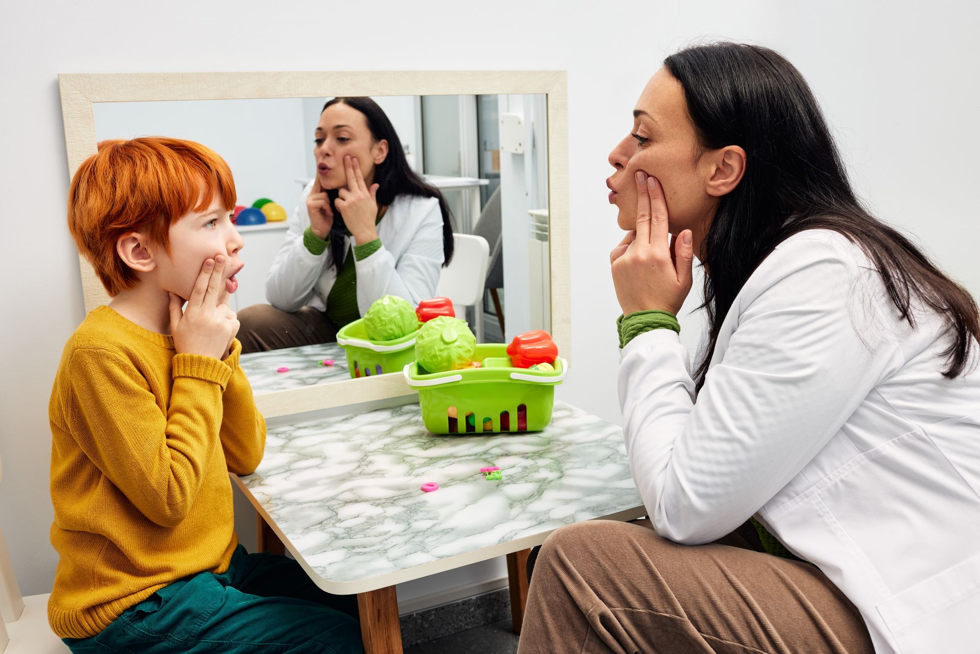 Child and therapist practicing facial exercises in front of a mirror.