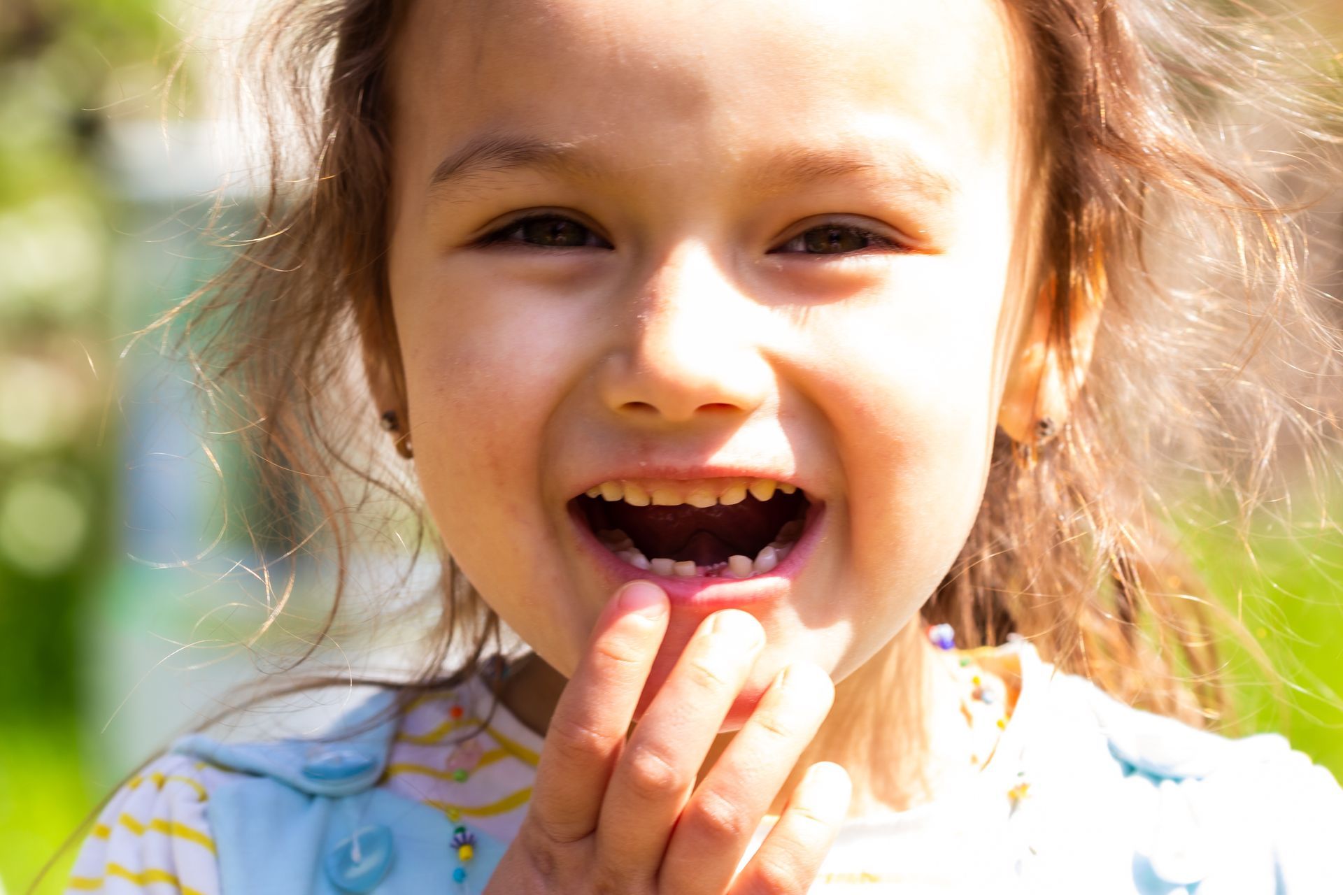 Young girl with missing front tooth, smiling, outdoors.