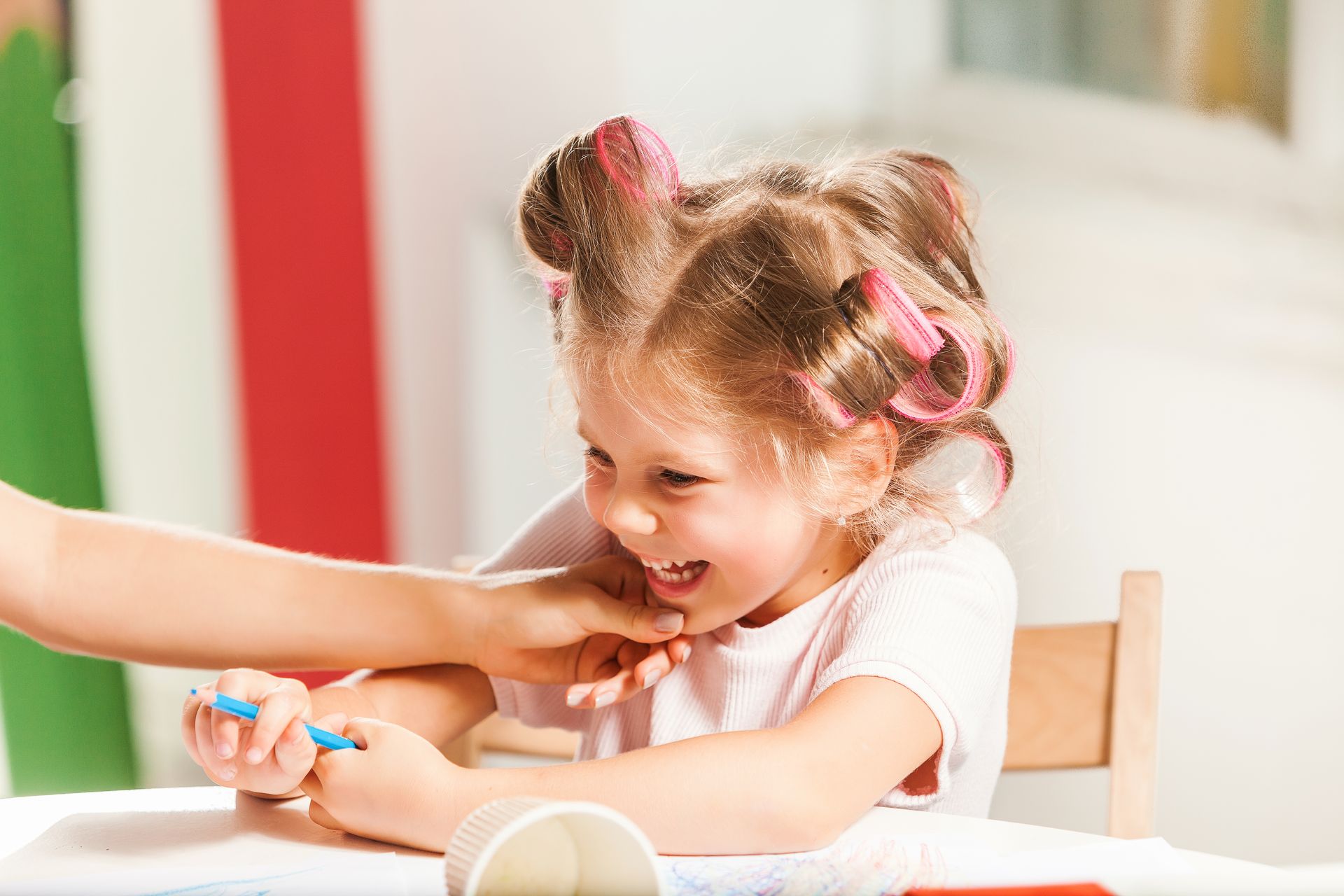 Girl with hair rollers laughs while someone holds a blue object near her mouth.