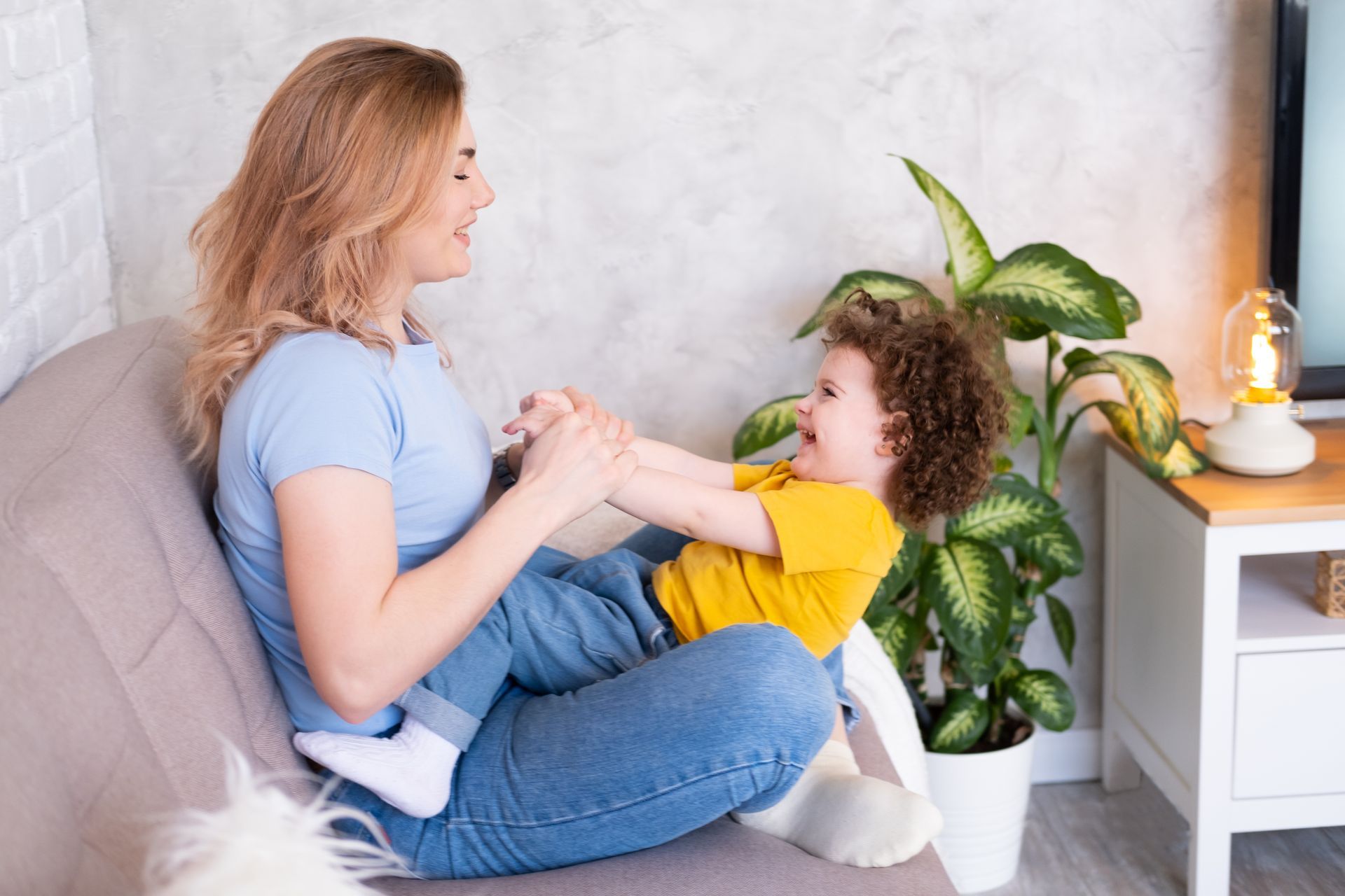 Woman sitting with child on her lap, playing and smiling on a couch, indoors.