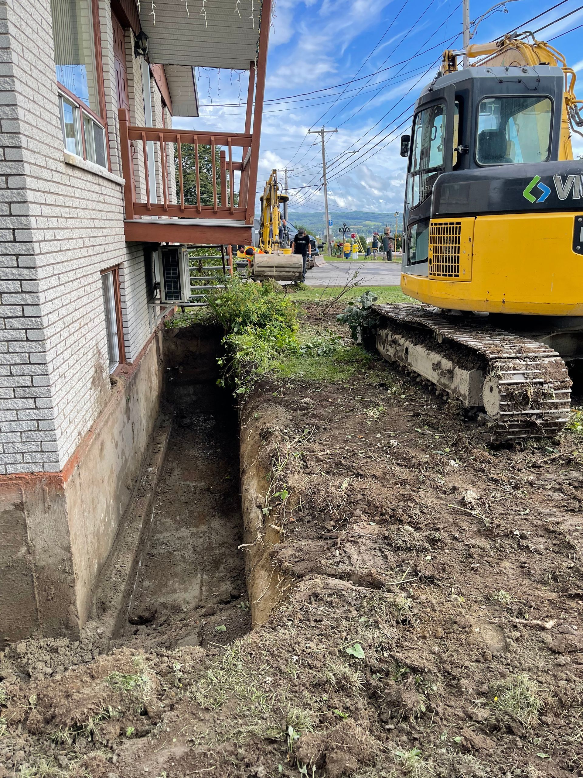 Une excavatrice jaune creuse un trou devant un bâtiment en briques.