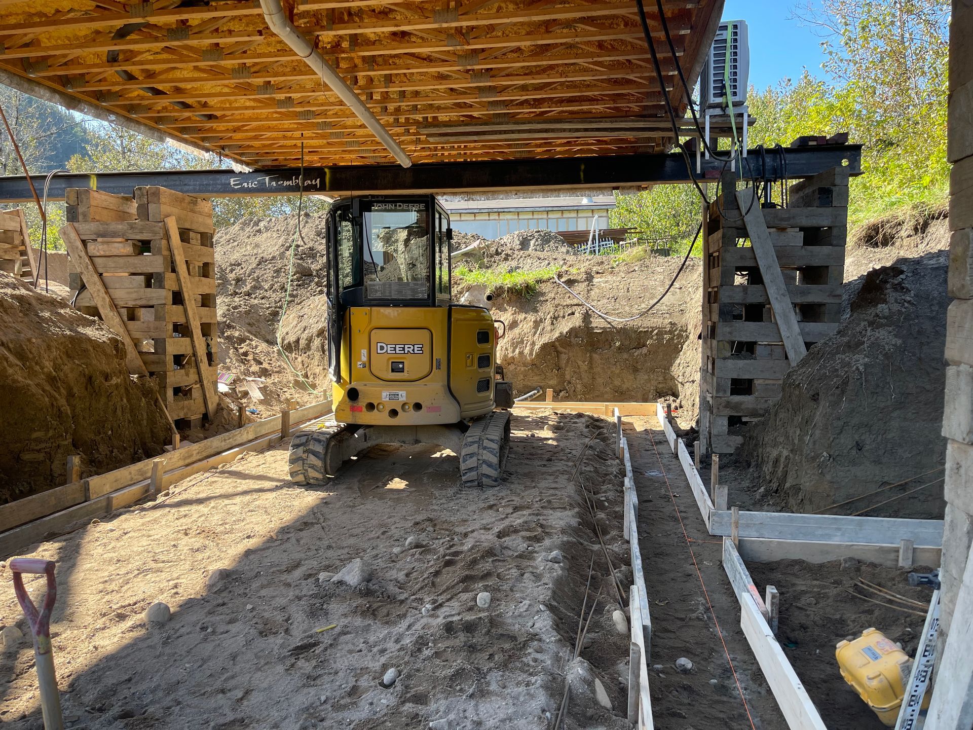 Une excavatrice jaune est assise sous une structure en bois.
