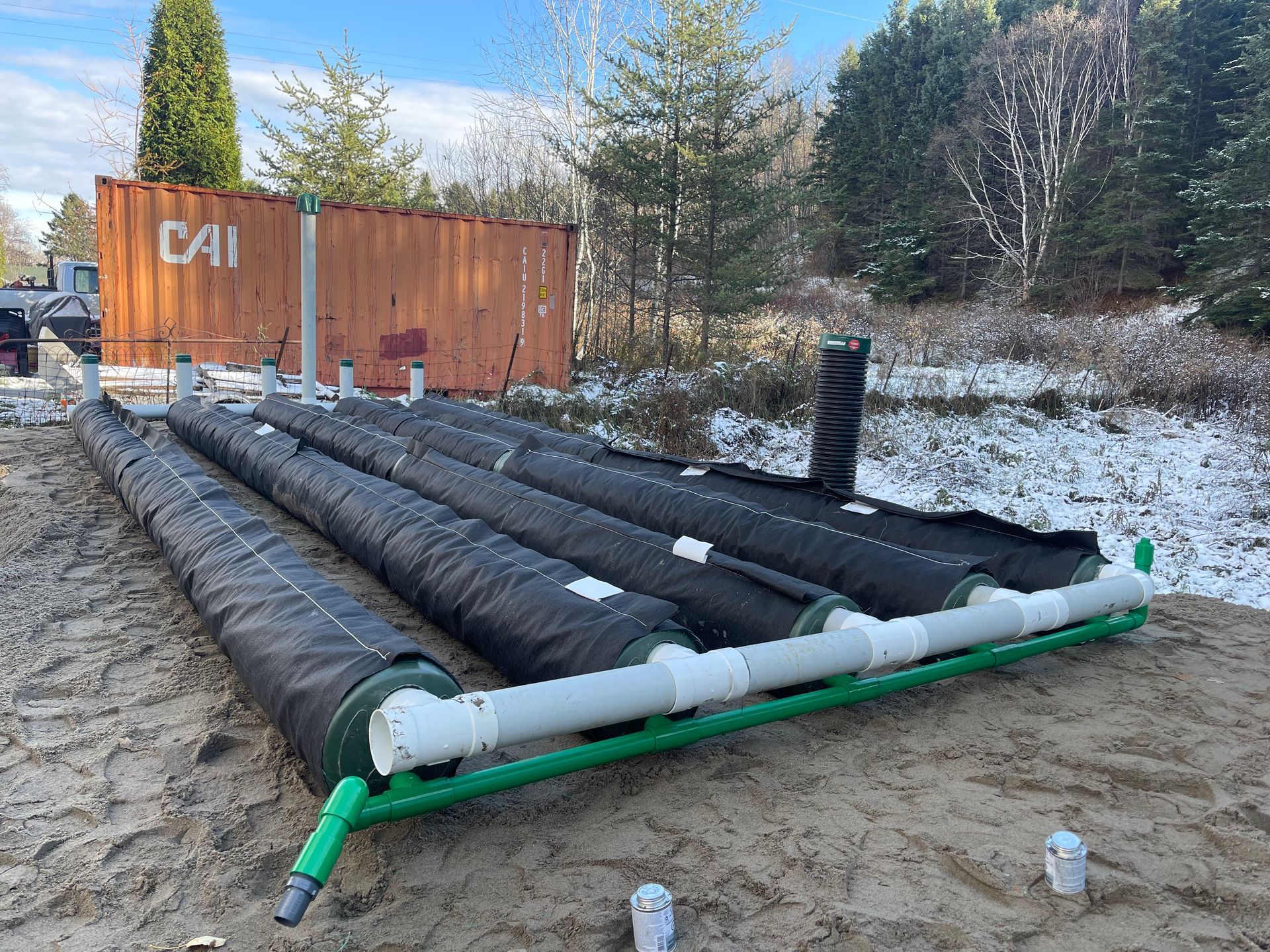 Un tas de tuyaux posés sur un terrain en terre à côté d'un conteneur d'expédition.