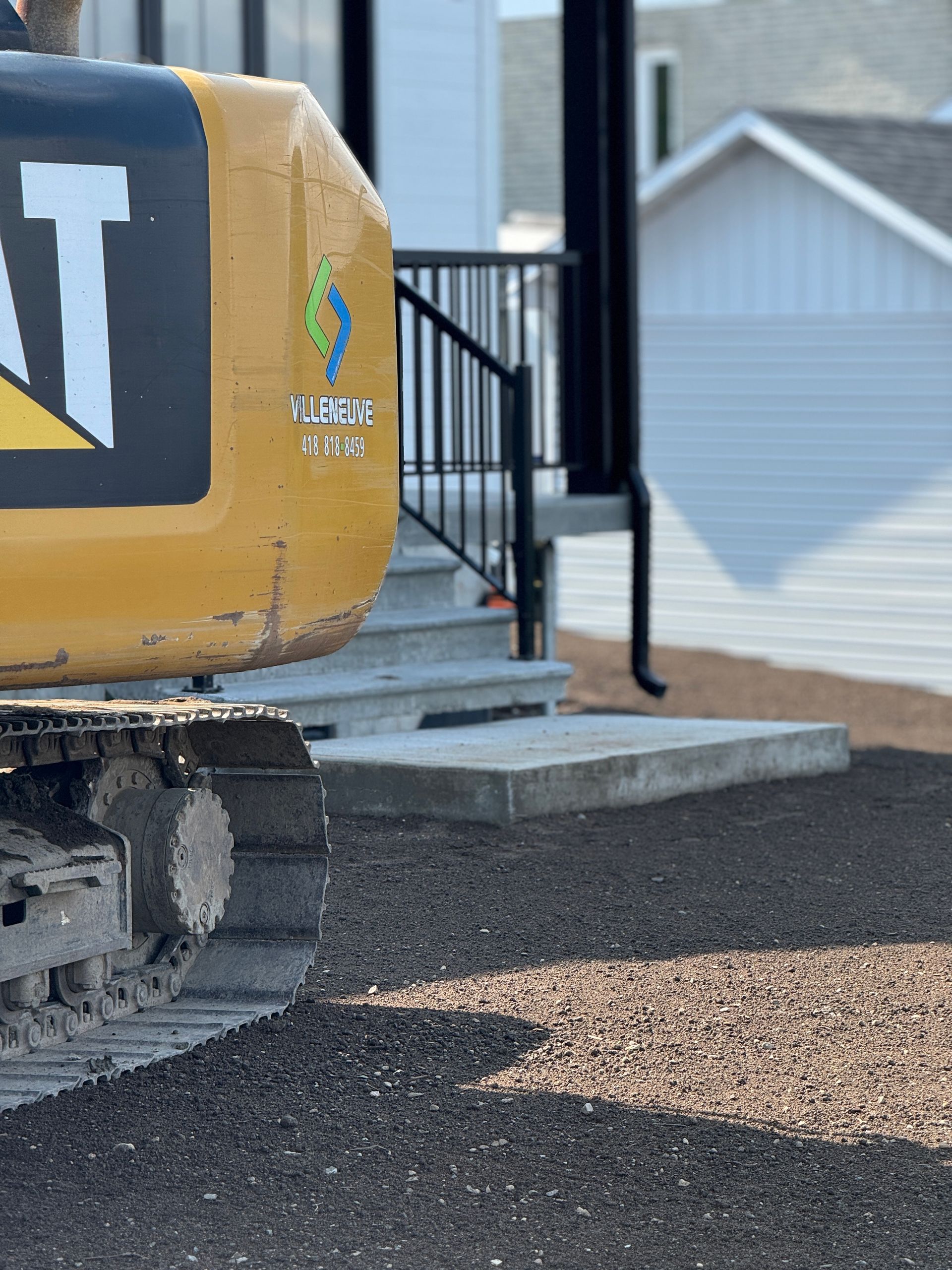 Une excavatrice jaune et noire est garée devant une maison.