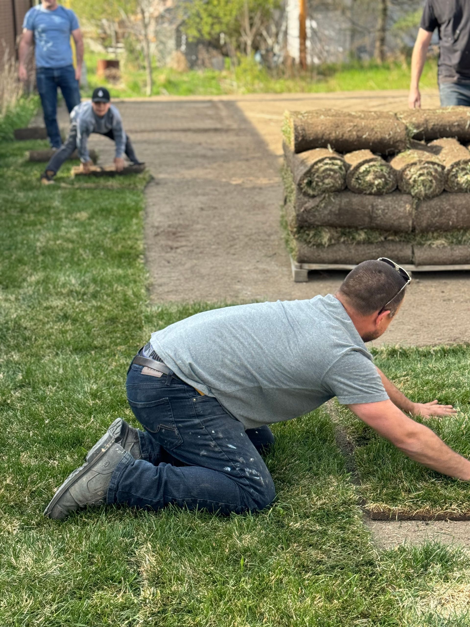 Un homme est agenouillé sur l'herbe devant une pile de rouleaux de gazon.