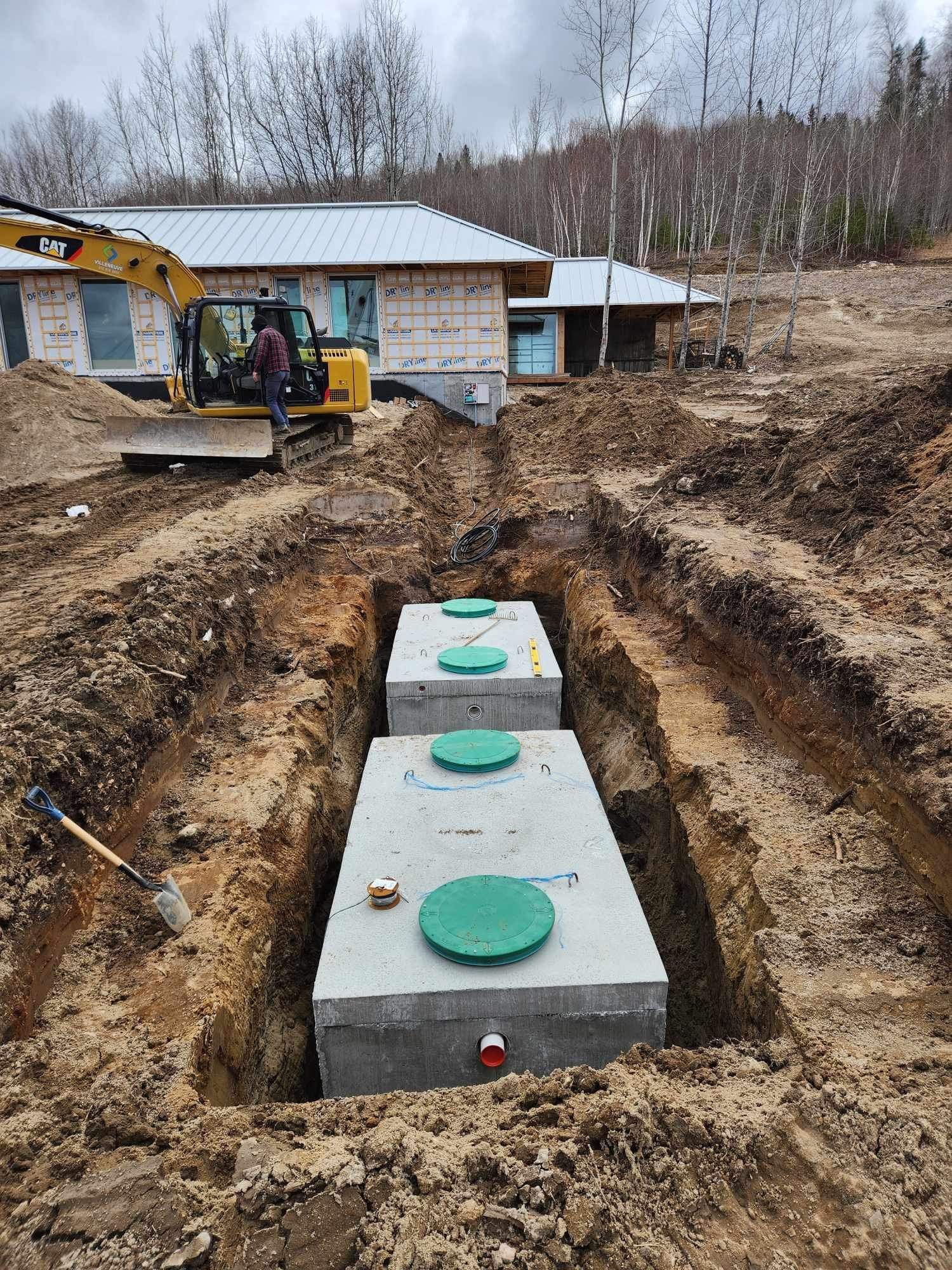 Une fosse septique est en cours de construction dans la terre devant une maison.