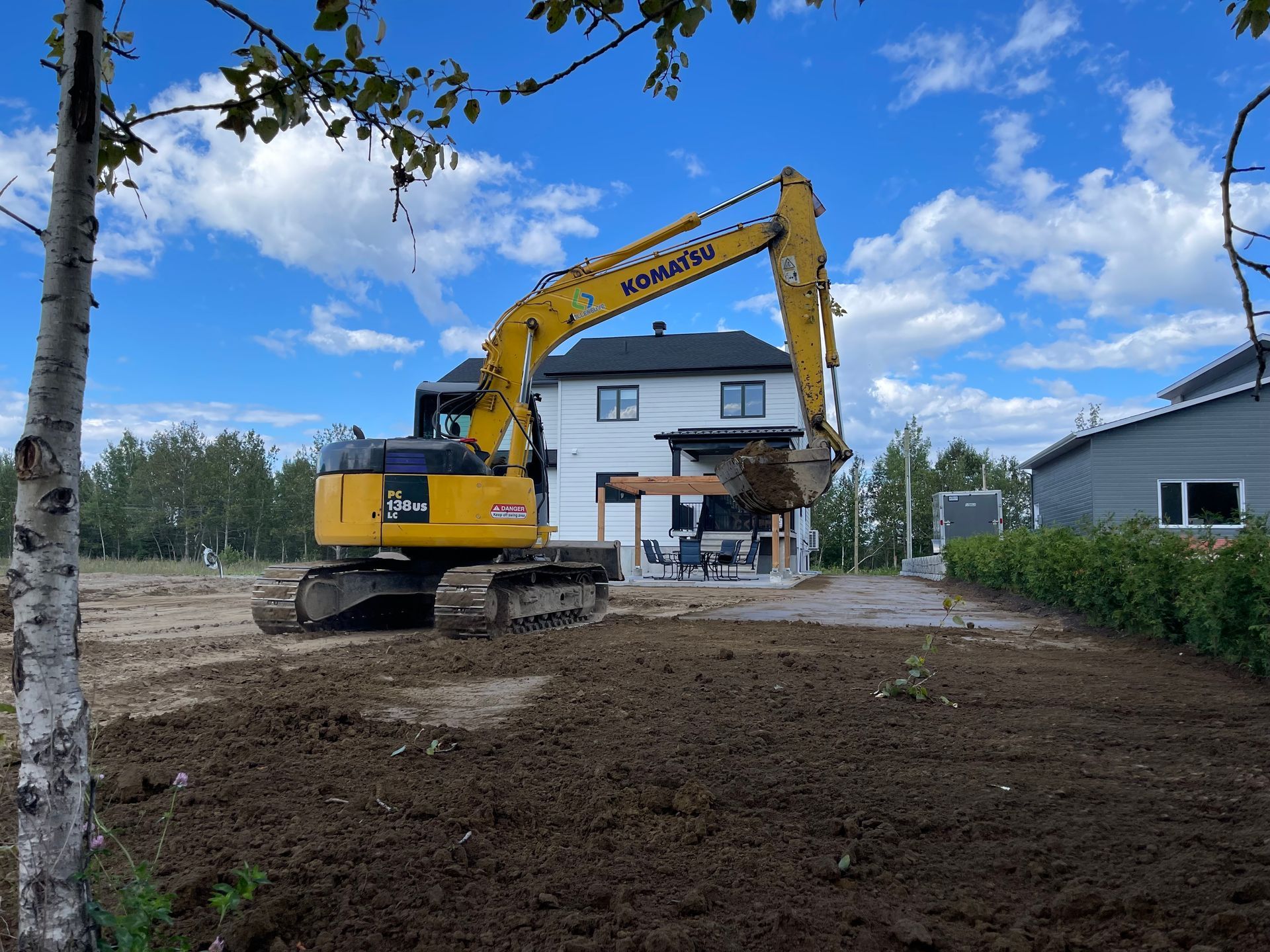 Une excavatrice Komatsu creuse dans la terre devant une maison