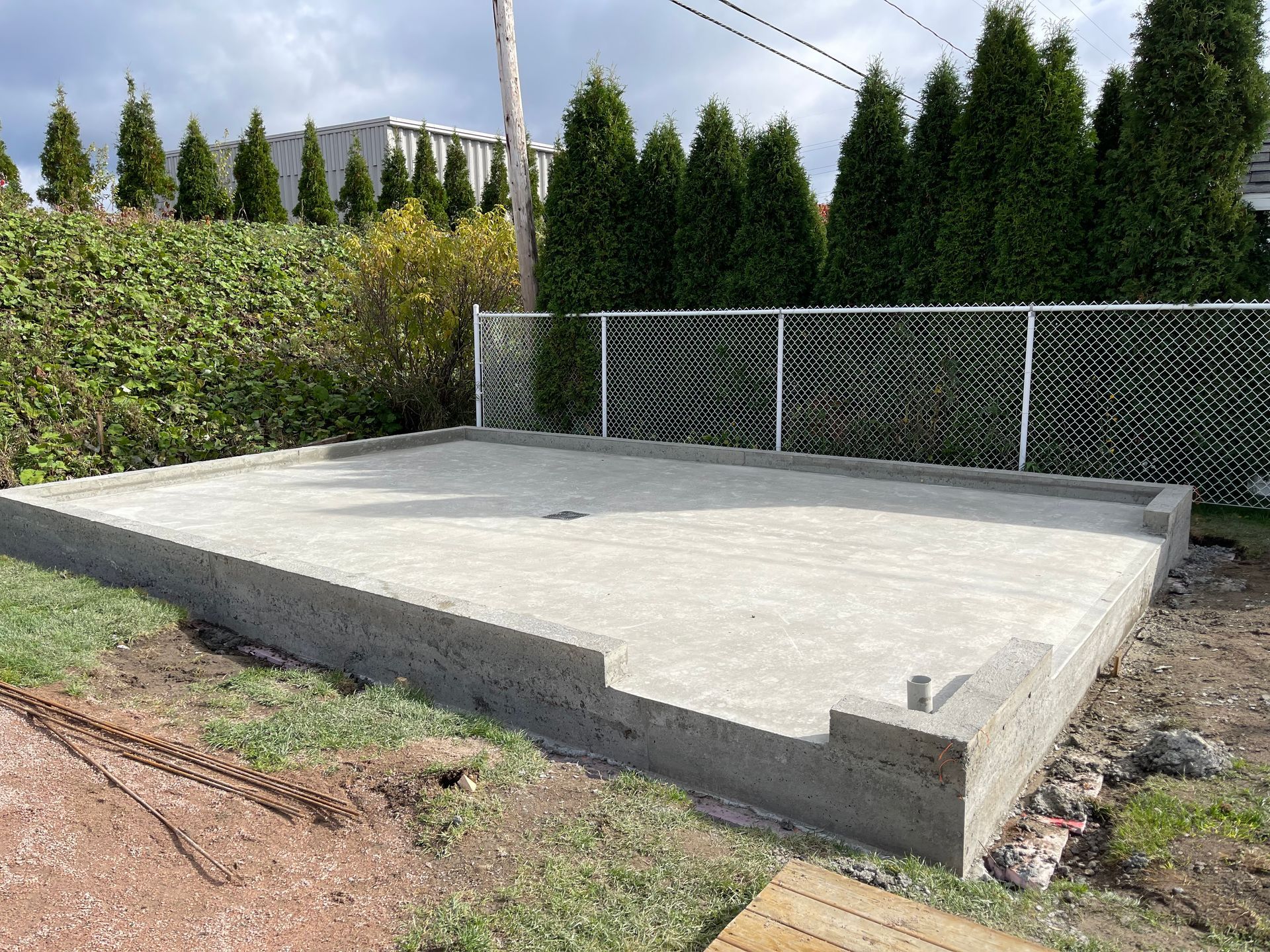 Une fondation en béton est en cours de construction dans une cour arrière à côté d'une clôture grillagée.