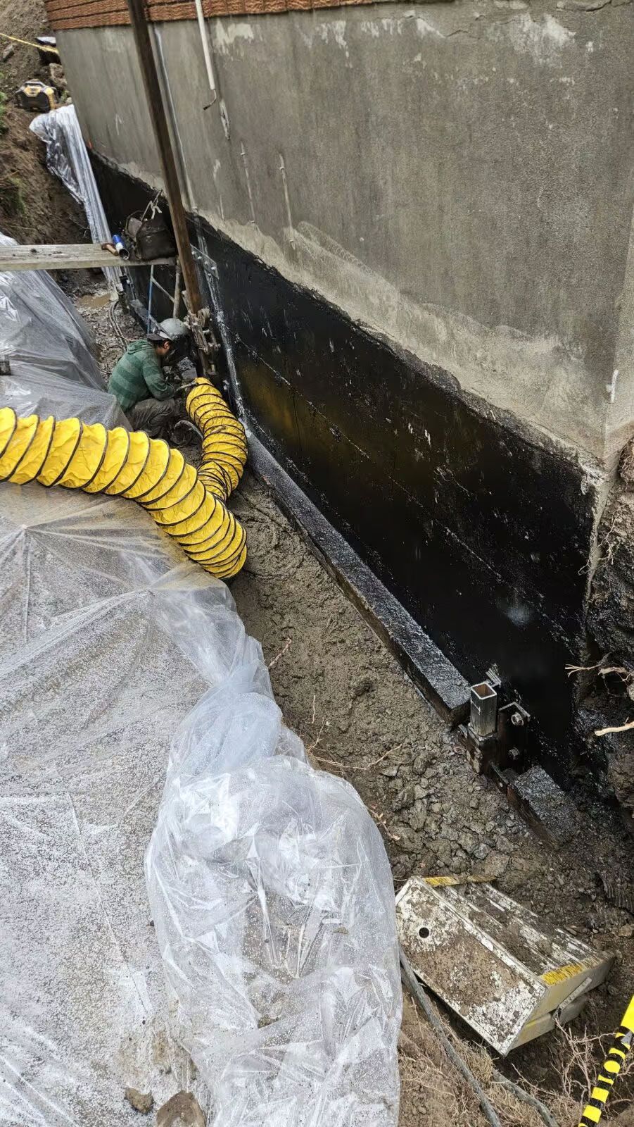 Mur du sous-sol recouvert d'un mastic noir, excavation, tuyau jaune.