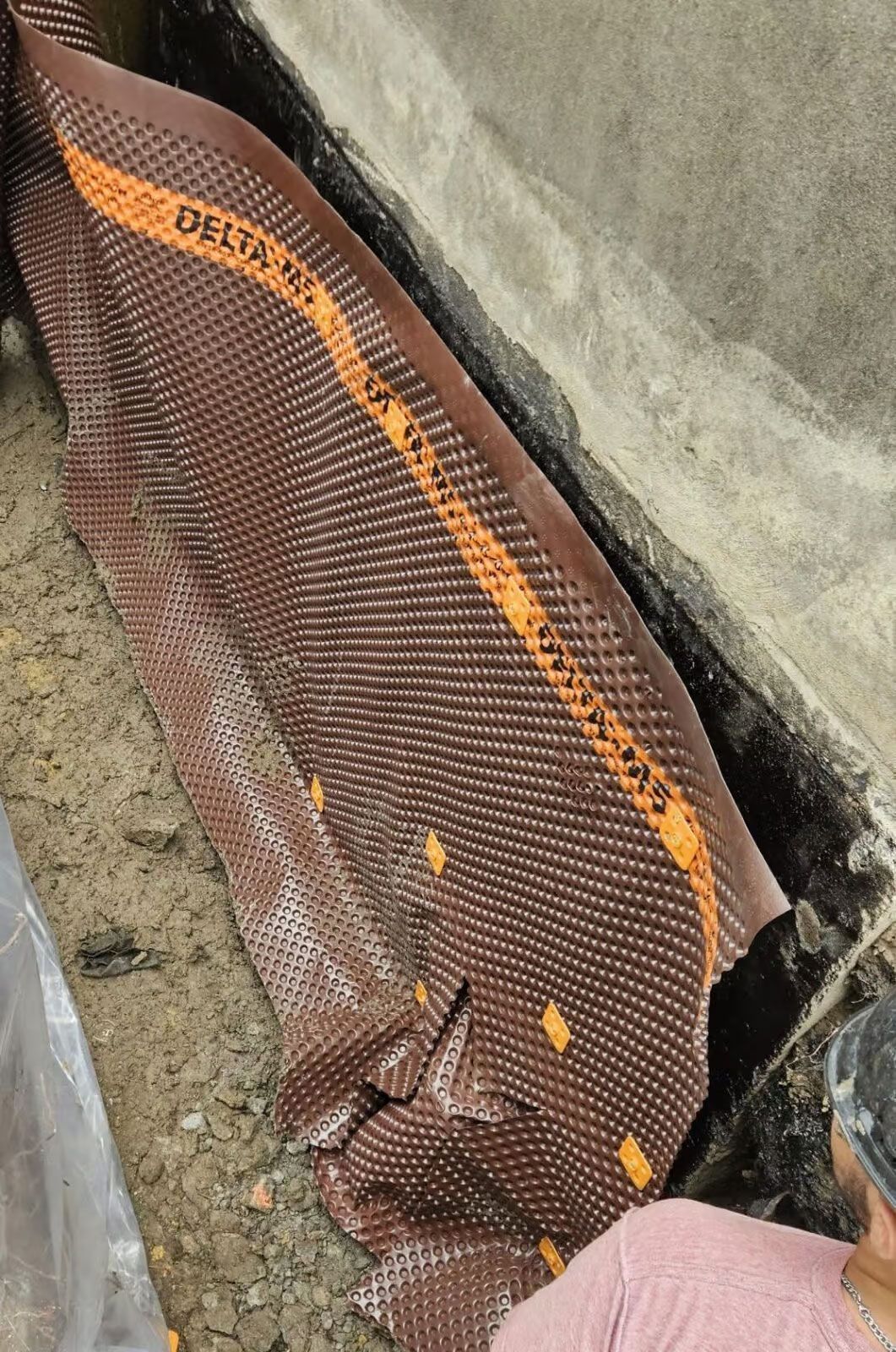 Membrane Delta-MS brune et orange installée dans une tranchée en béton pour le drainage.