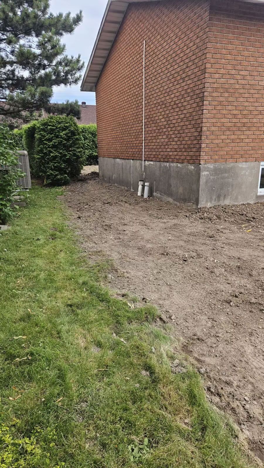 Un bâtiment en briques avec des fondations en béton, une zone de terre et une pelouse.