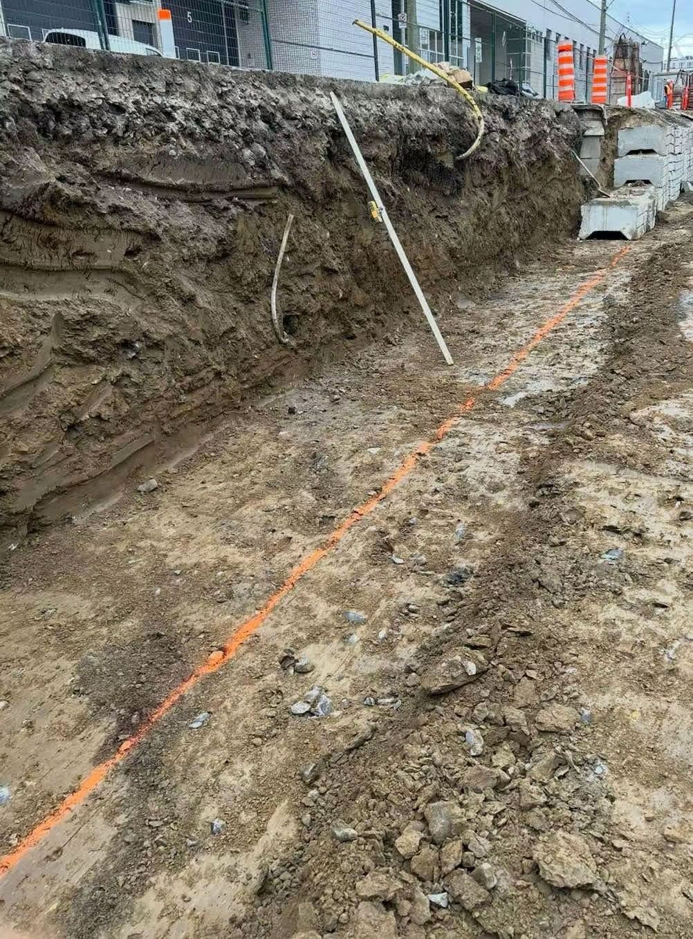 Chantier avec une tranchée ouverte, une ligne de marquage orange et des outils.